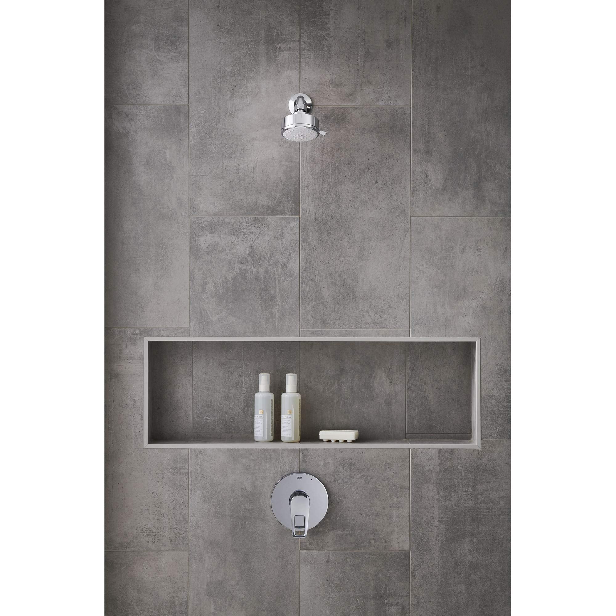 Chrome pressure balance valve trim with round escutcheon plate mounted on gray tile bathroom wall below overhead showerhead.