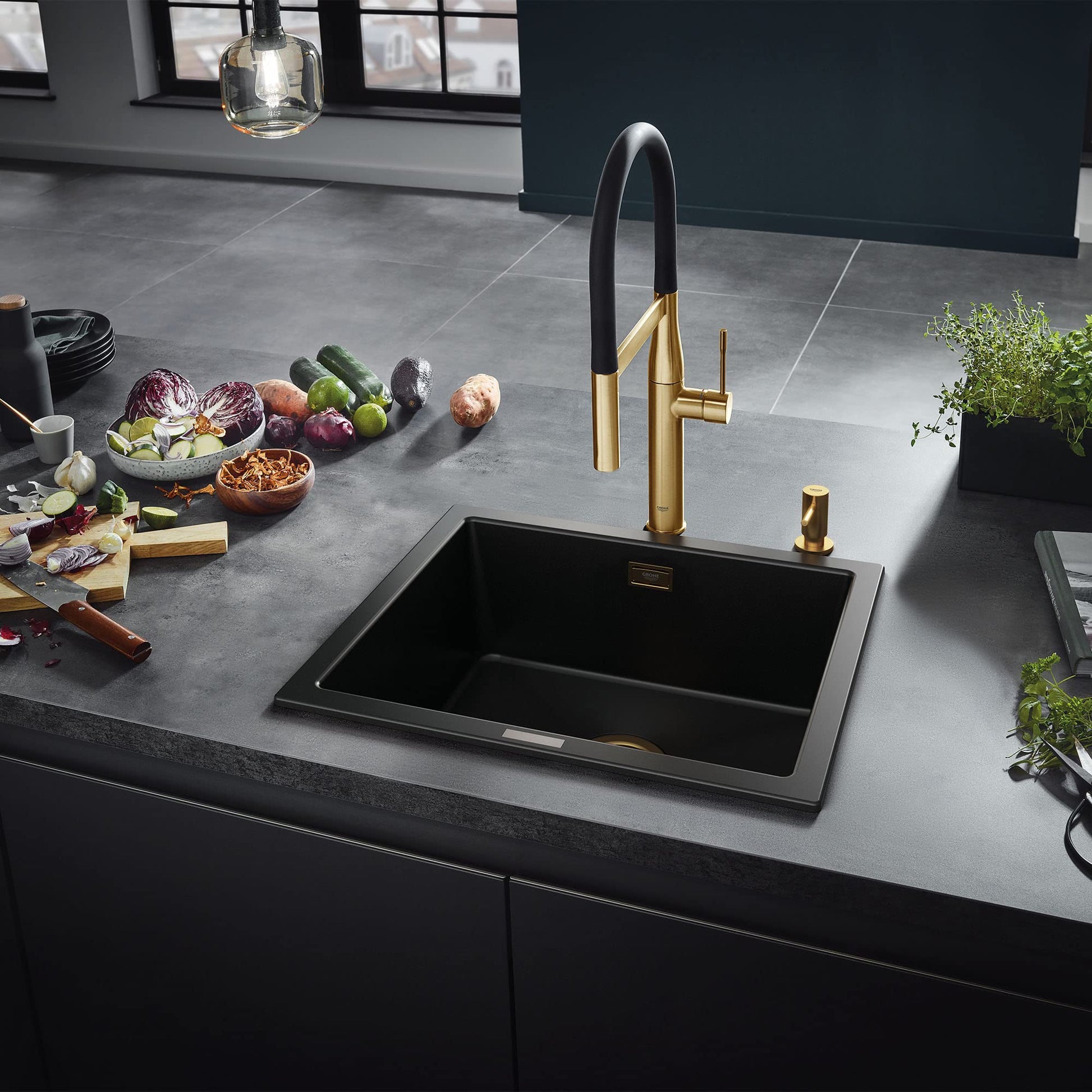Grohe Essence kitchen faucet with black curved spout and gold accents mounted above black sink on gray countertop.