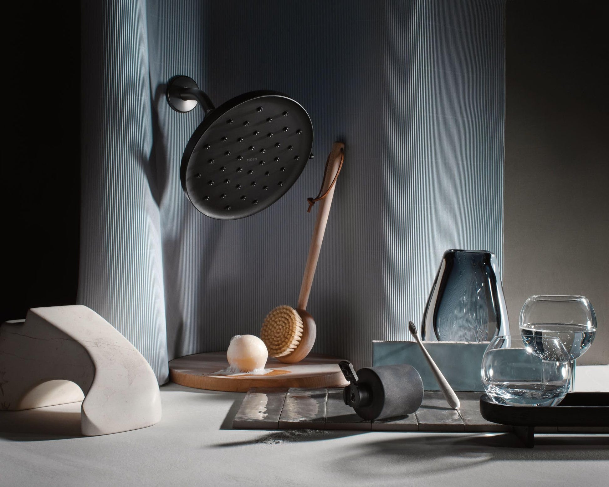 Matte black round rainshower head with multiple spray holes mounted on textured gray wall.