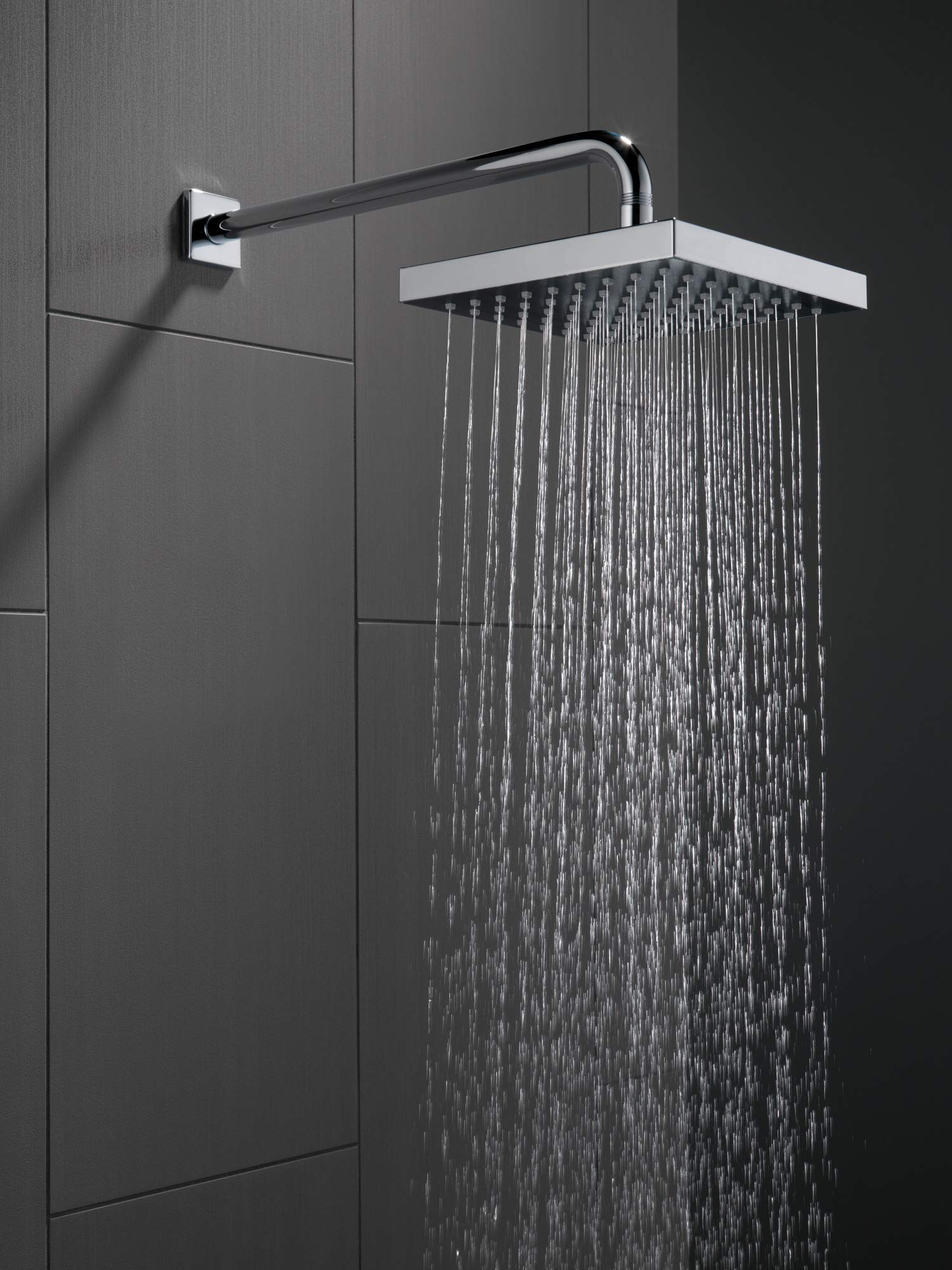 Black stainless steel shower flange with curved arm mounted to gray tile wall, white rectangular showerhead with water stream