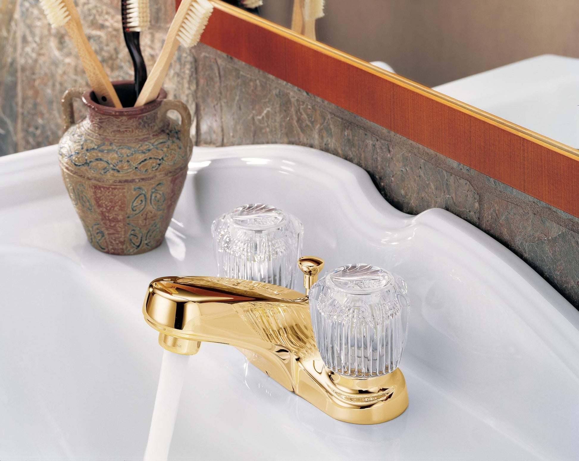 Gold-tone centerset bathroom faucet with two clear knob handles and pop-up drain on white sink.
