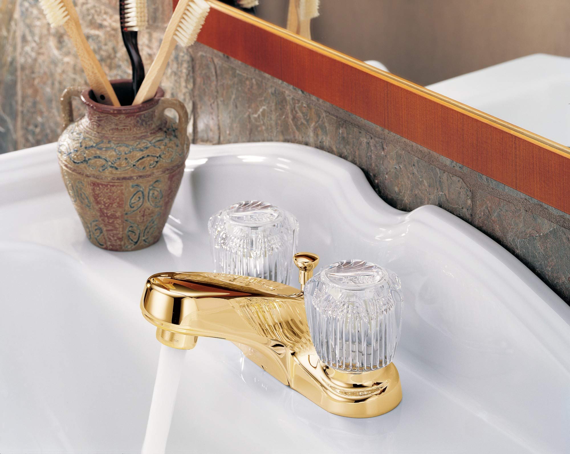 Gold-tone centerset bathroom faucet with two clear knob handles and pop-up drain on white sink.