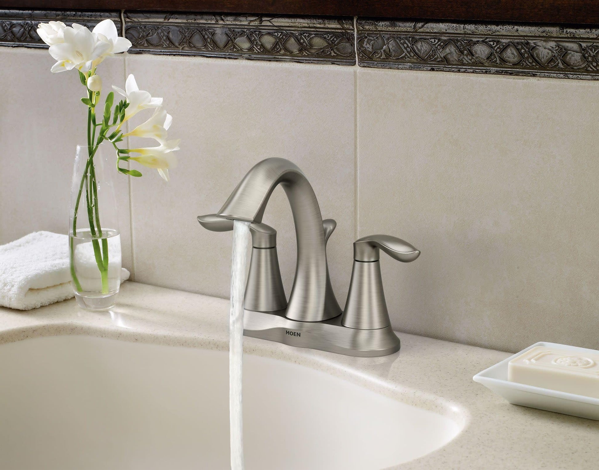 Brushed nickel two-handle bathroom faucet with curved spout installed on beige sink countertop.