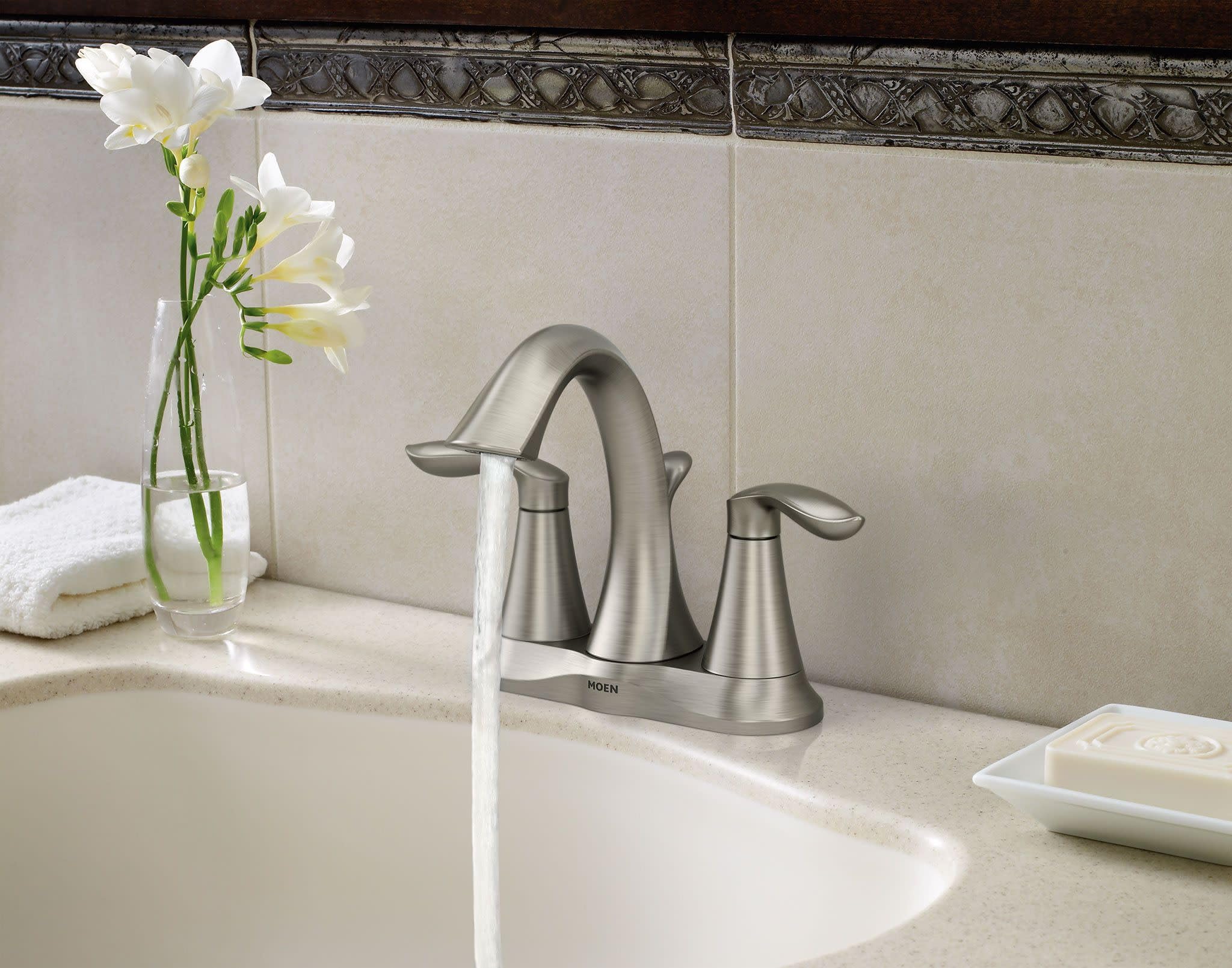 Brushed nickel two-handle bathroom faucet with curved spout installed on beige sink countertop.