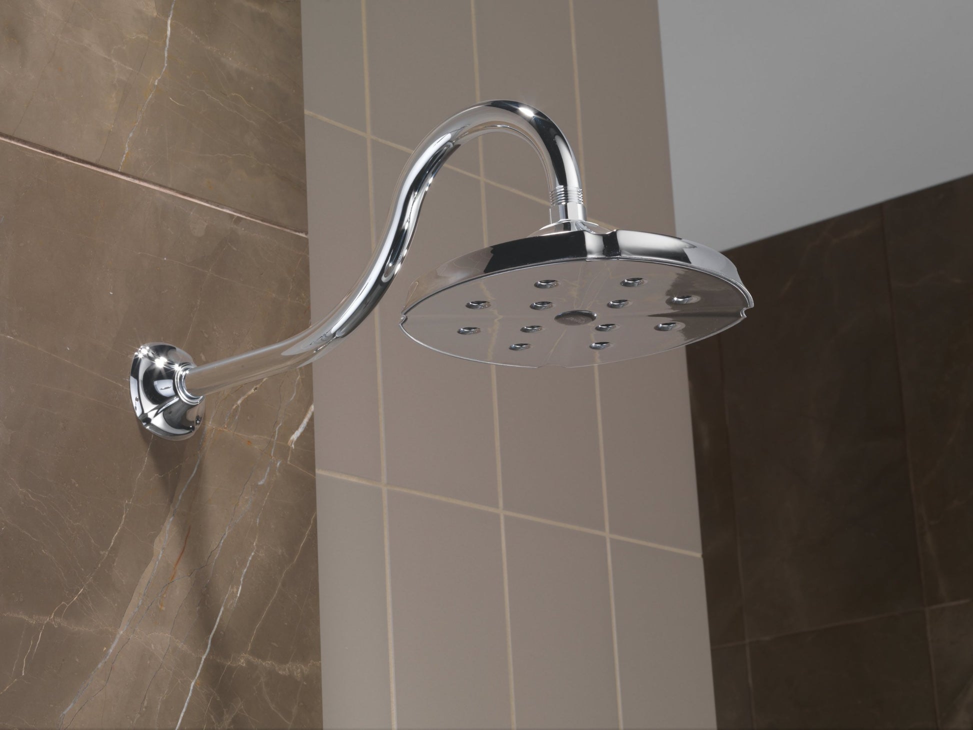 Chrome shower head with curved arm and wall-mounted flange against tiled bathroom wall.