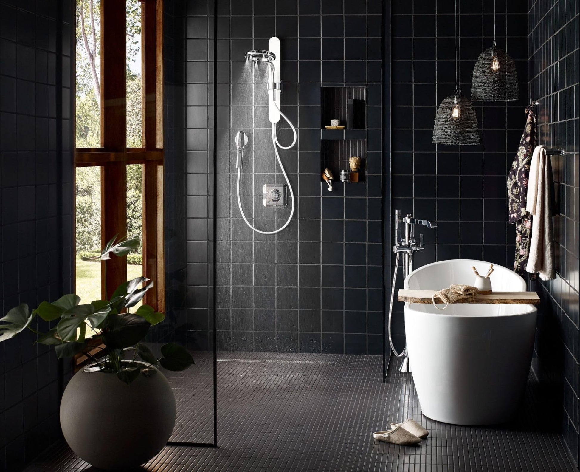 Chrome freestanding tub filler with single handle and detachable handshower mounted on bathroom wall above white soaking tub.