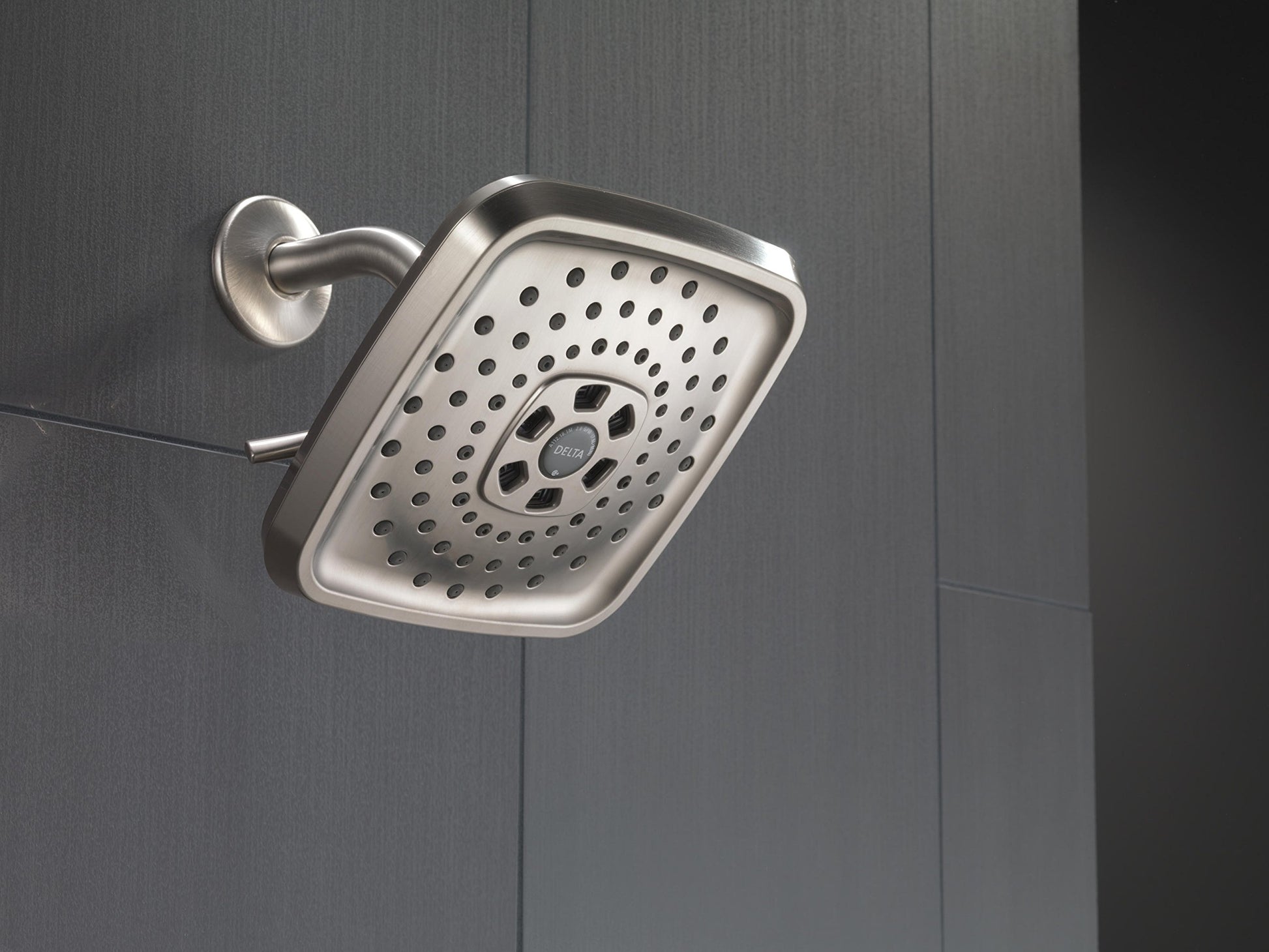Stainless steel rectangular shower head with perforated spray pattern mounted on wall with curved arm.
