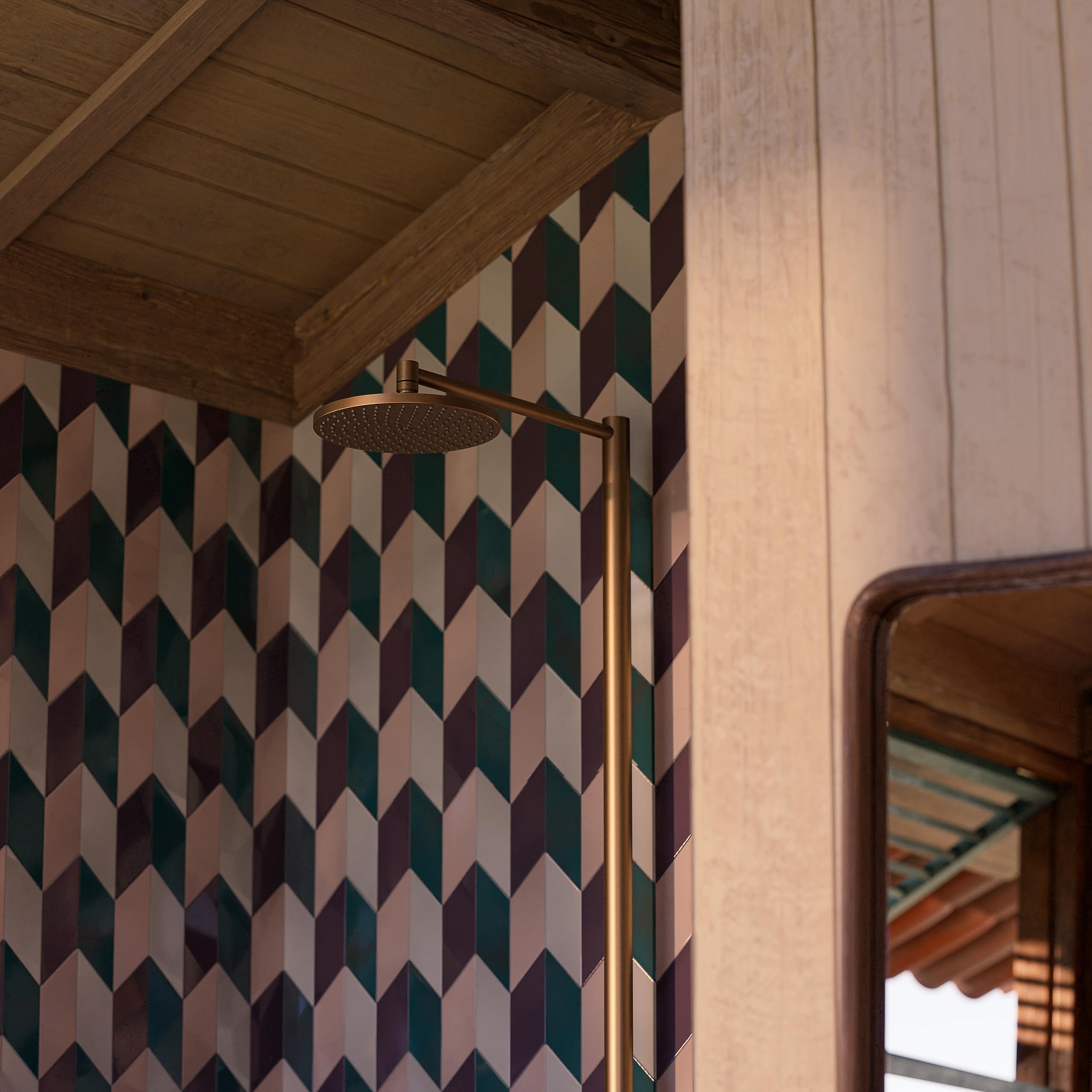 Brushed black chrome showerhead mounted on angled brass pipe against geometric patterned wall tiles.