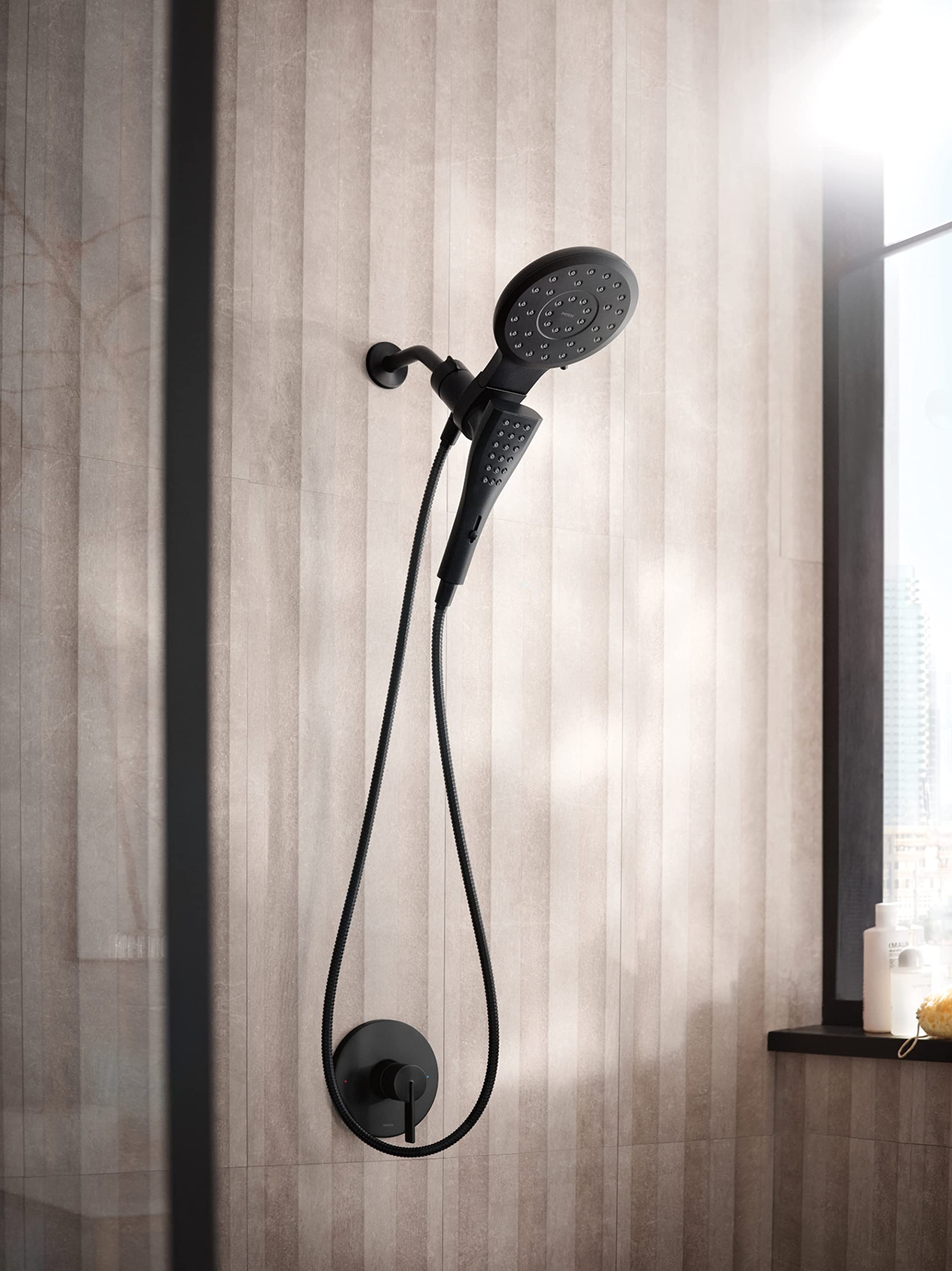 Matte black showerhead with handheld spray unit connected by hose mounted on bathroom tile wall.