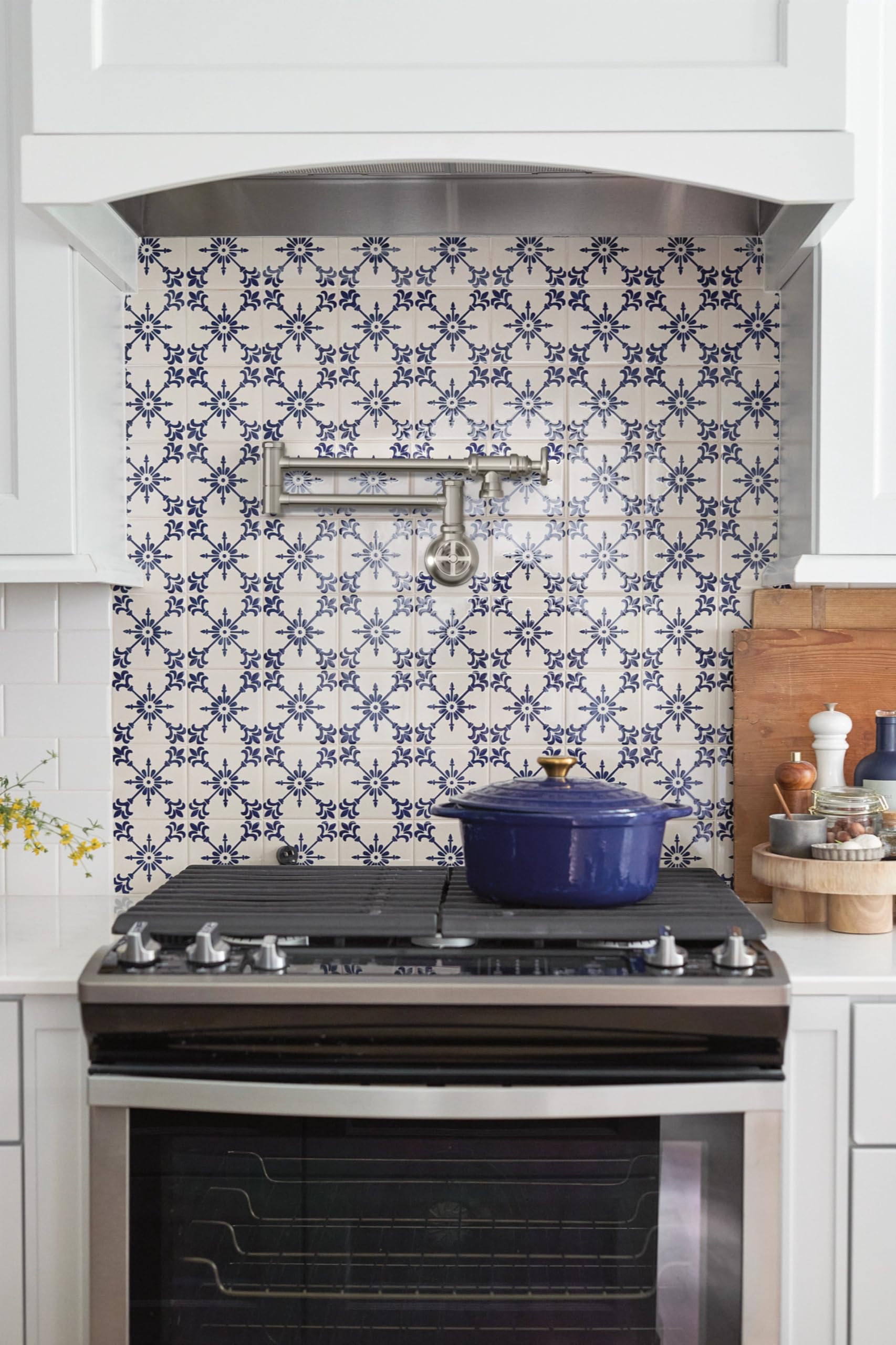 Stainless steel wall-mount pot filler faucet with swing arm folded horizontally above stovetop.