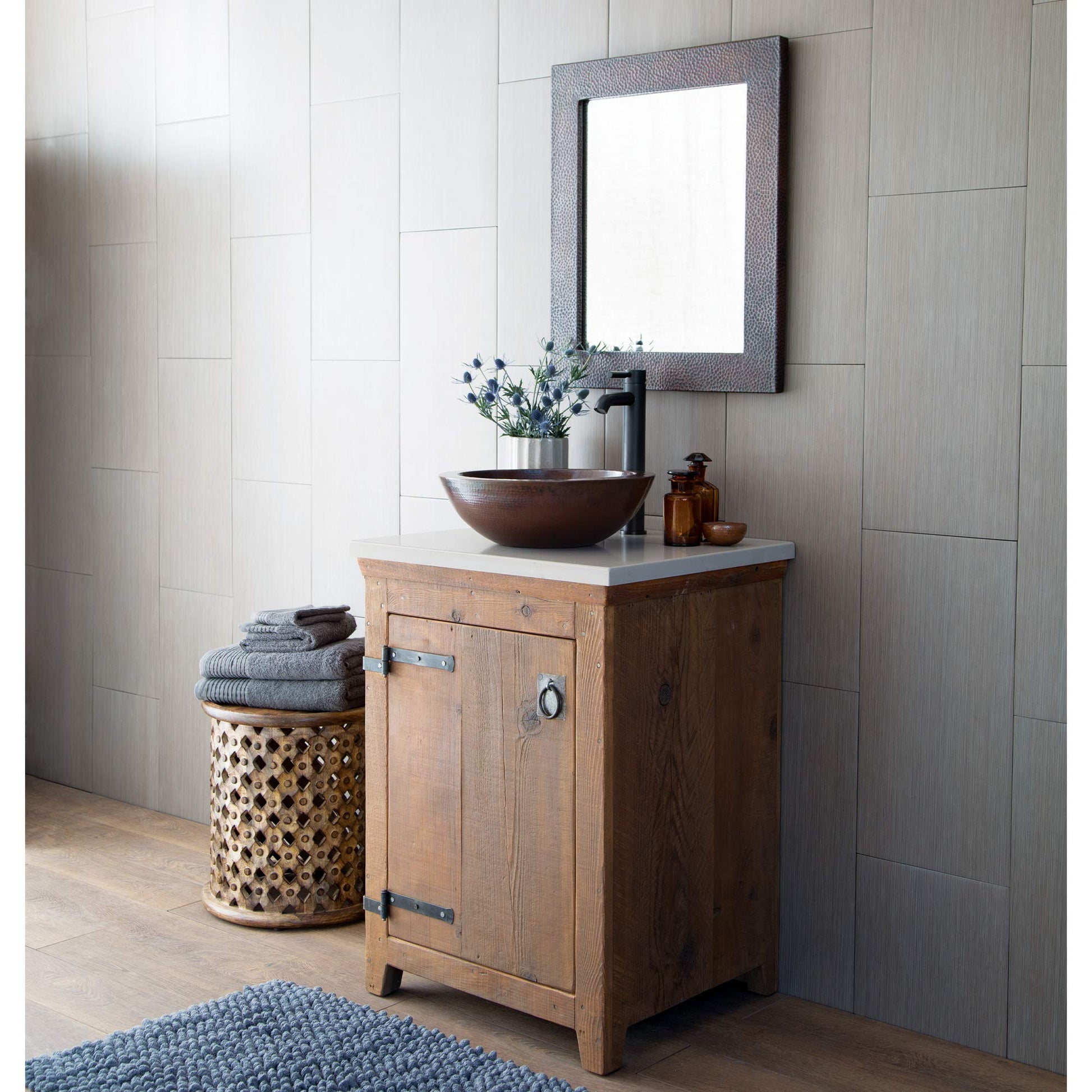 Rectangular mirror with textured gray-brown frame hung above a wooden bathroom vanity with vessel sink.