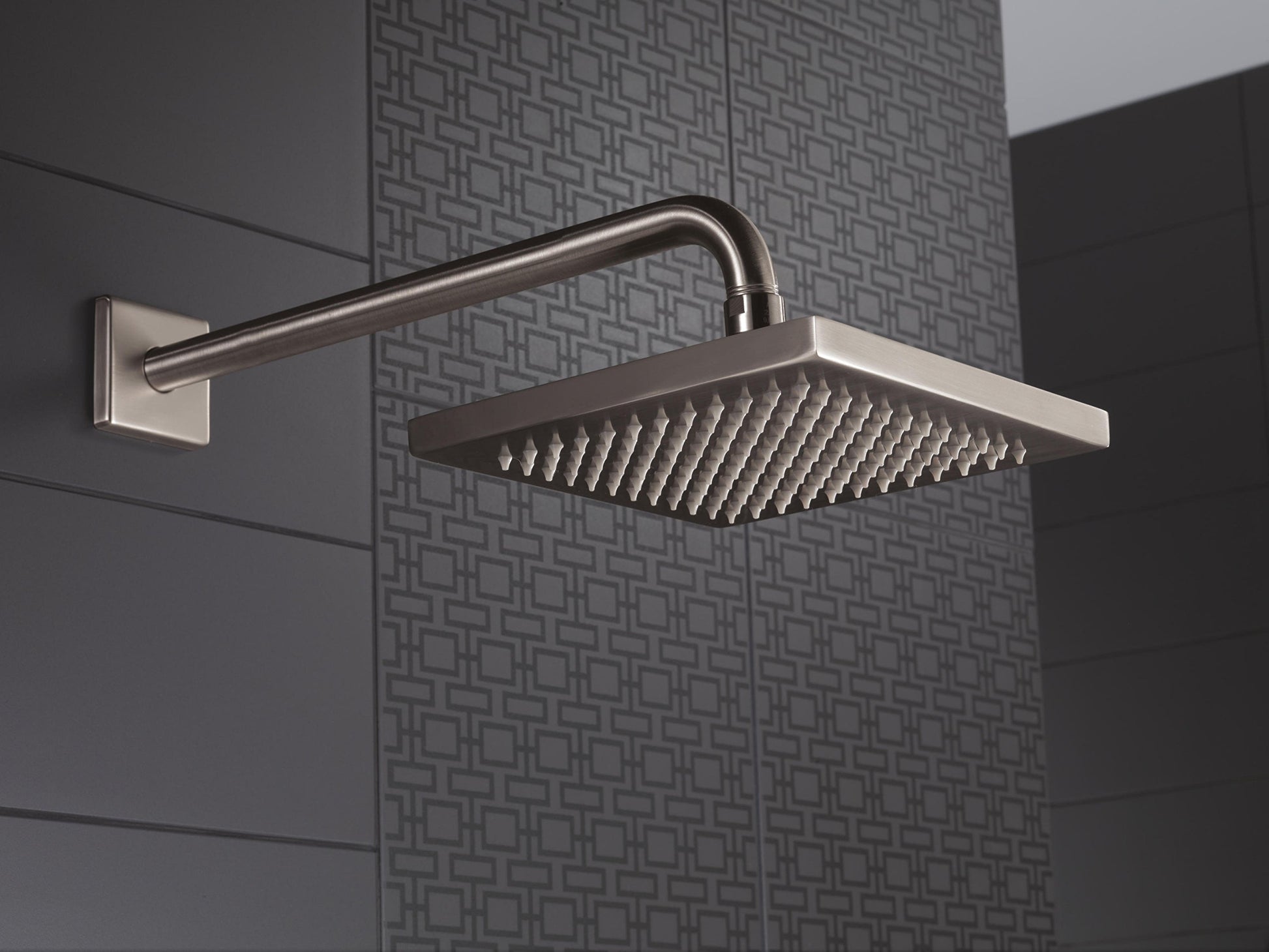 Stainless steel shower arm with square rainfall showerhead mounted on tile wall.