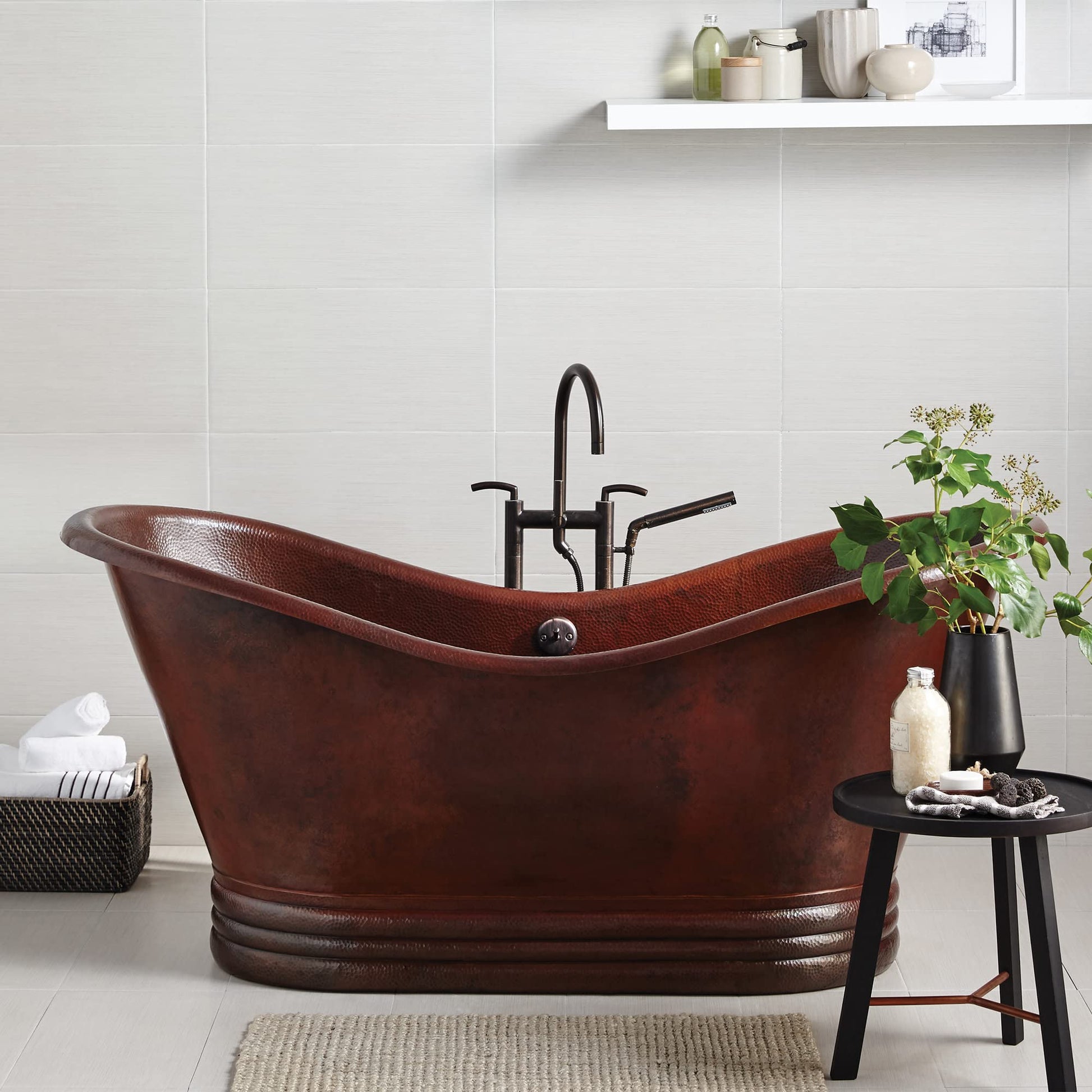 Hammered copper freestanding bathtub with curved sides and dark metal faucet in bathroom setting.