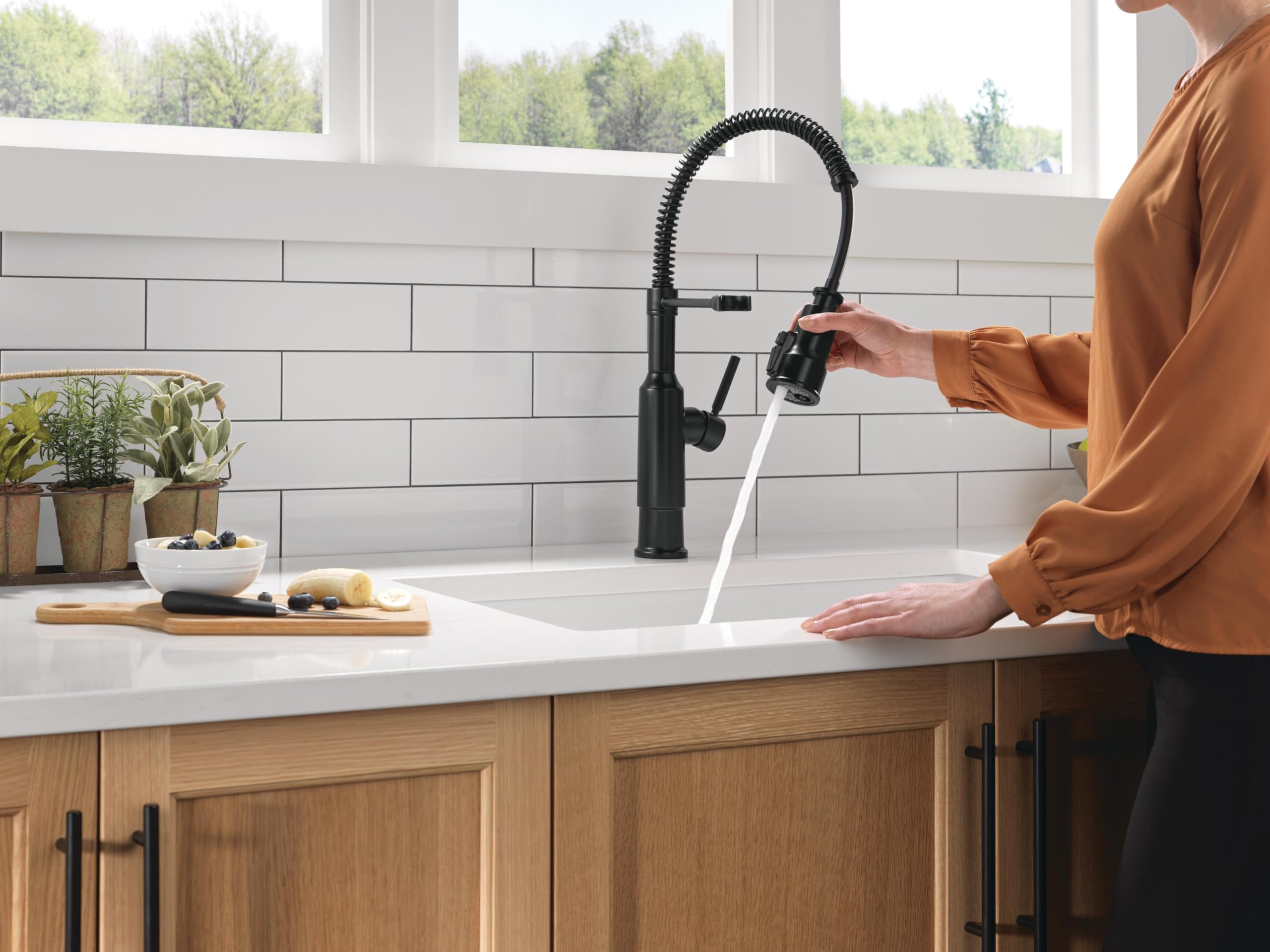 Matte black single-handle pull-down kitchen faucet with coiled hose installed above white sink in modern kitchen.
