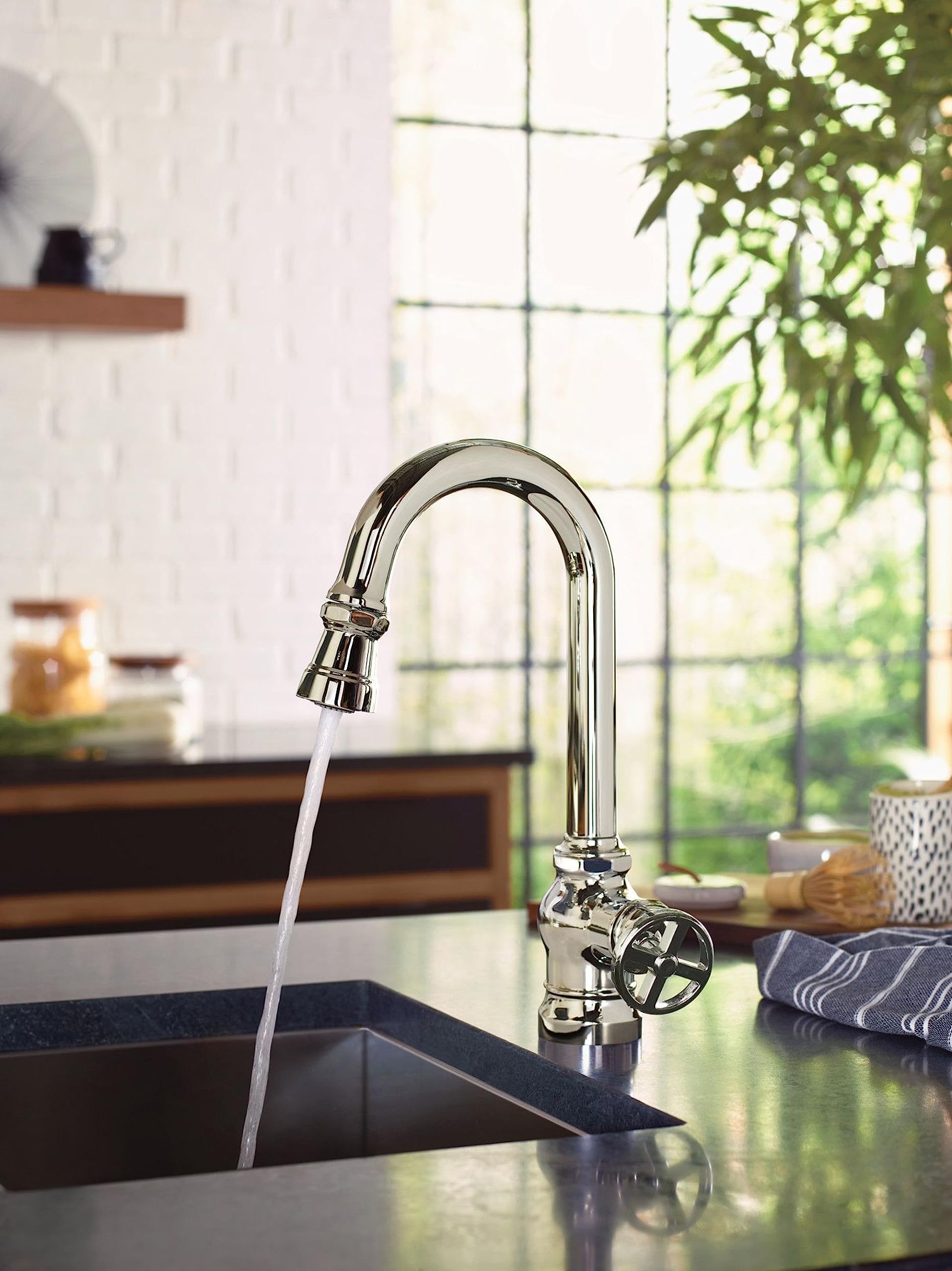 Chrome pulldown bar faucet with single handle mounted on kitchen sink counter with water flowing from spout.