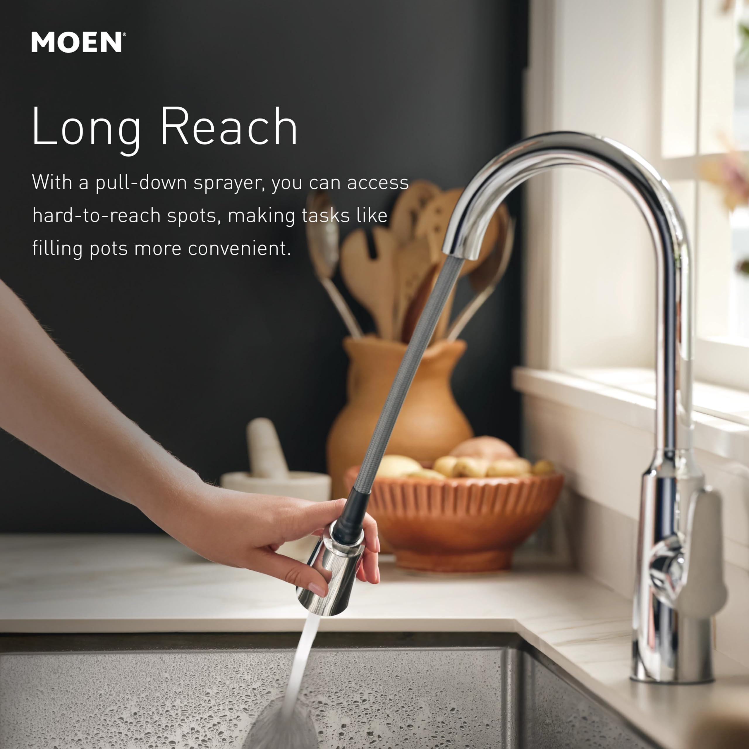 Stainless steel kitchen faucet with pull-down sprayer extended over sink, showing retractable spray head in use.