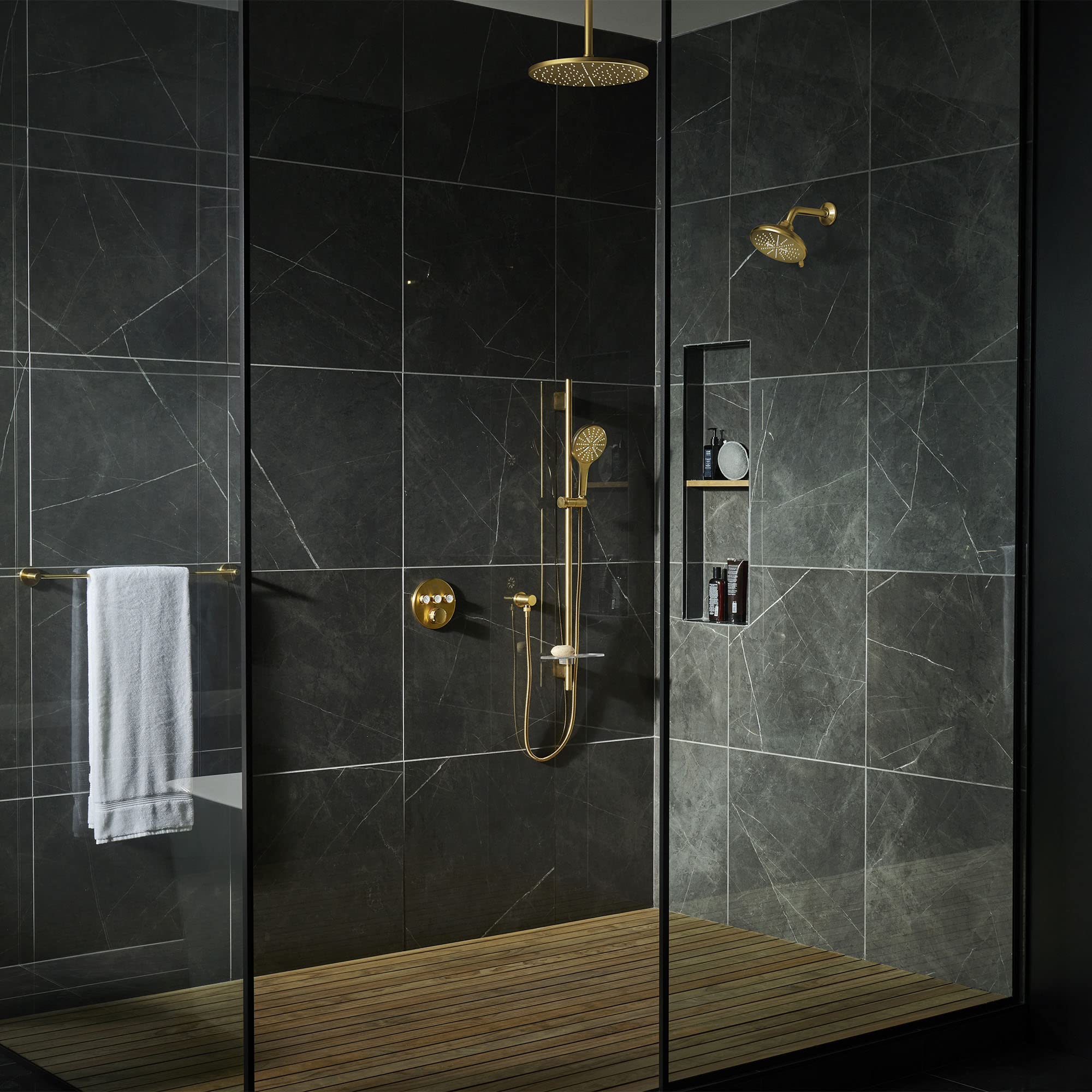 Grohe Rainshower 12" brushed gold ceiling shower arm mounted above dark marble bathroom tiles in modern shower enclosure.