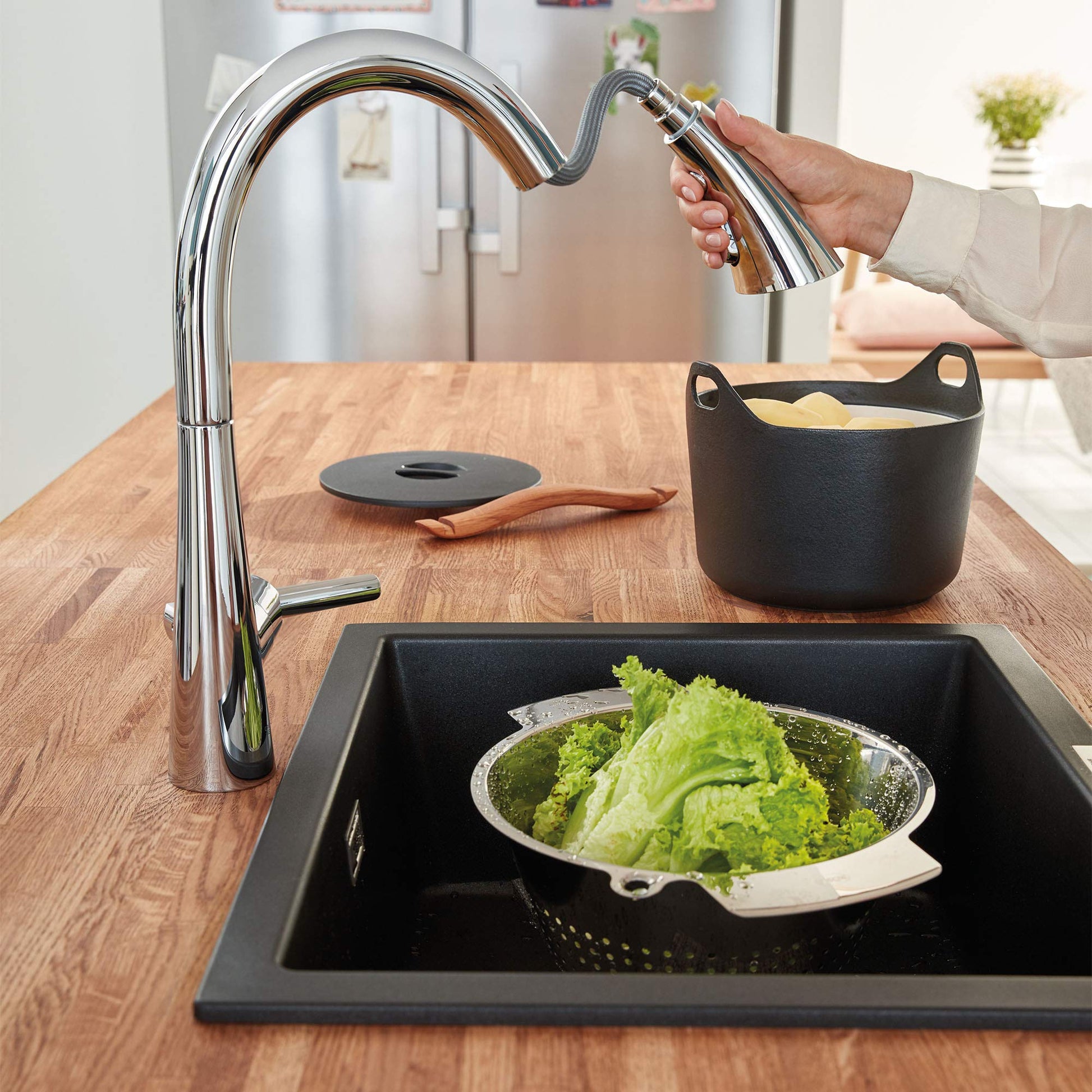 Chrome pull-down kitchen faucet with single handle and curved spout over black sink, with hand pulling spray head.