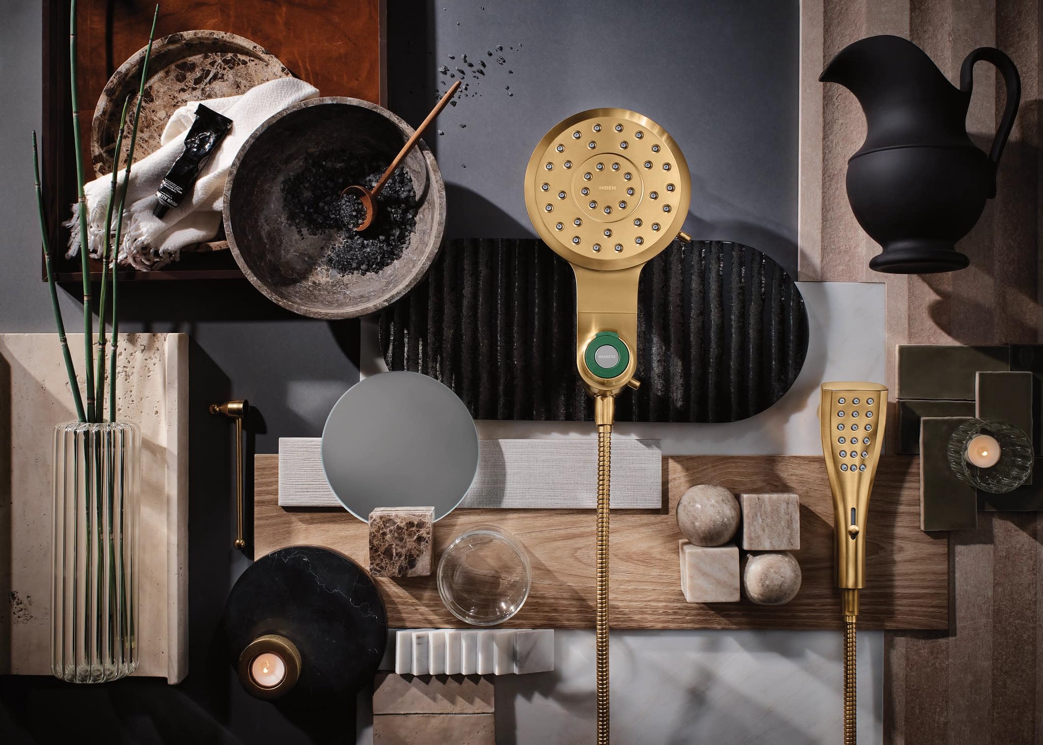 Brushed gold showerhead and handheld shower components displayed with decorative styling items on neutral background.