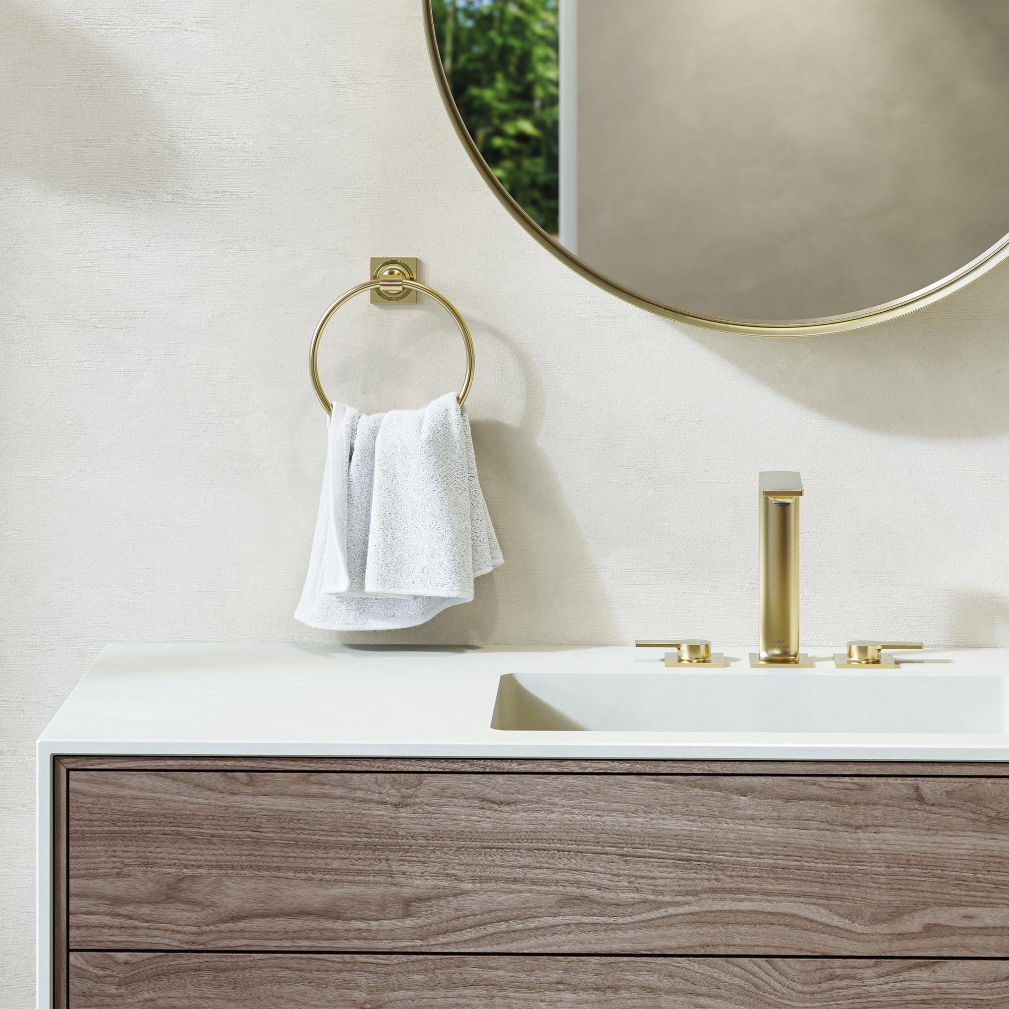 Brushed nickel circular towel ring mounted on bathroom wall above sink with white towel draped over it.