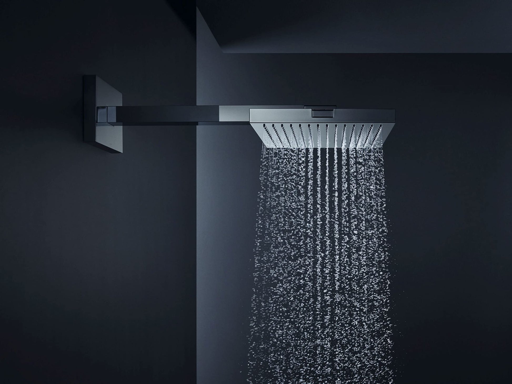 Brushed nickel square shower head mounted on arm with single-jet water stream against dark background.