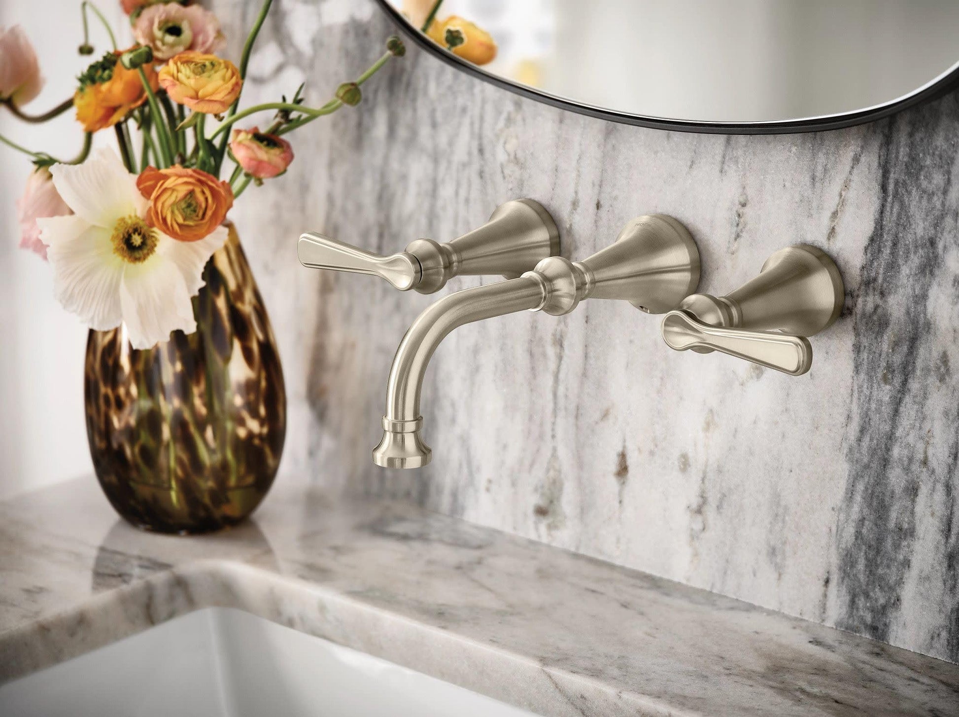 Brushed nickel wall-mounted bathroom faucet with two lever handles and curved spout installed above marble sink.
