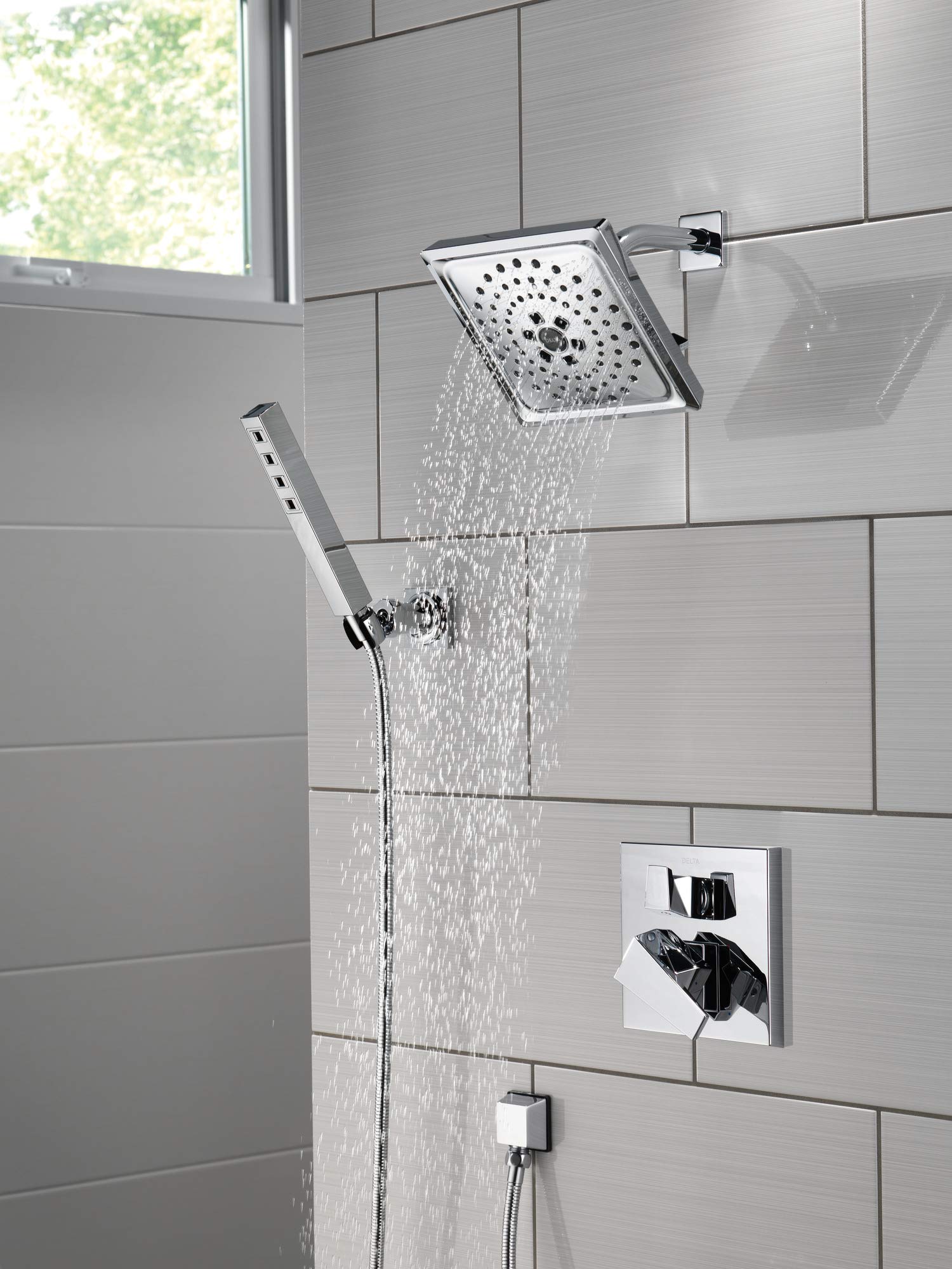 Black stainless steel shower arm mounted on tile wall with square showerhead and handheld spray attachment.