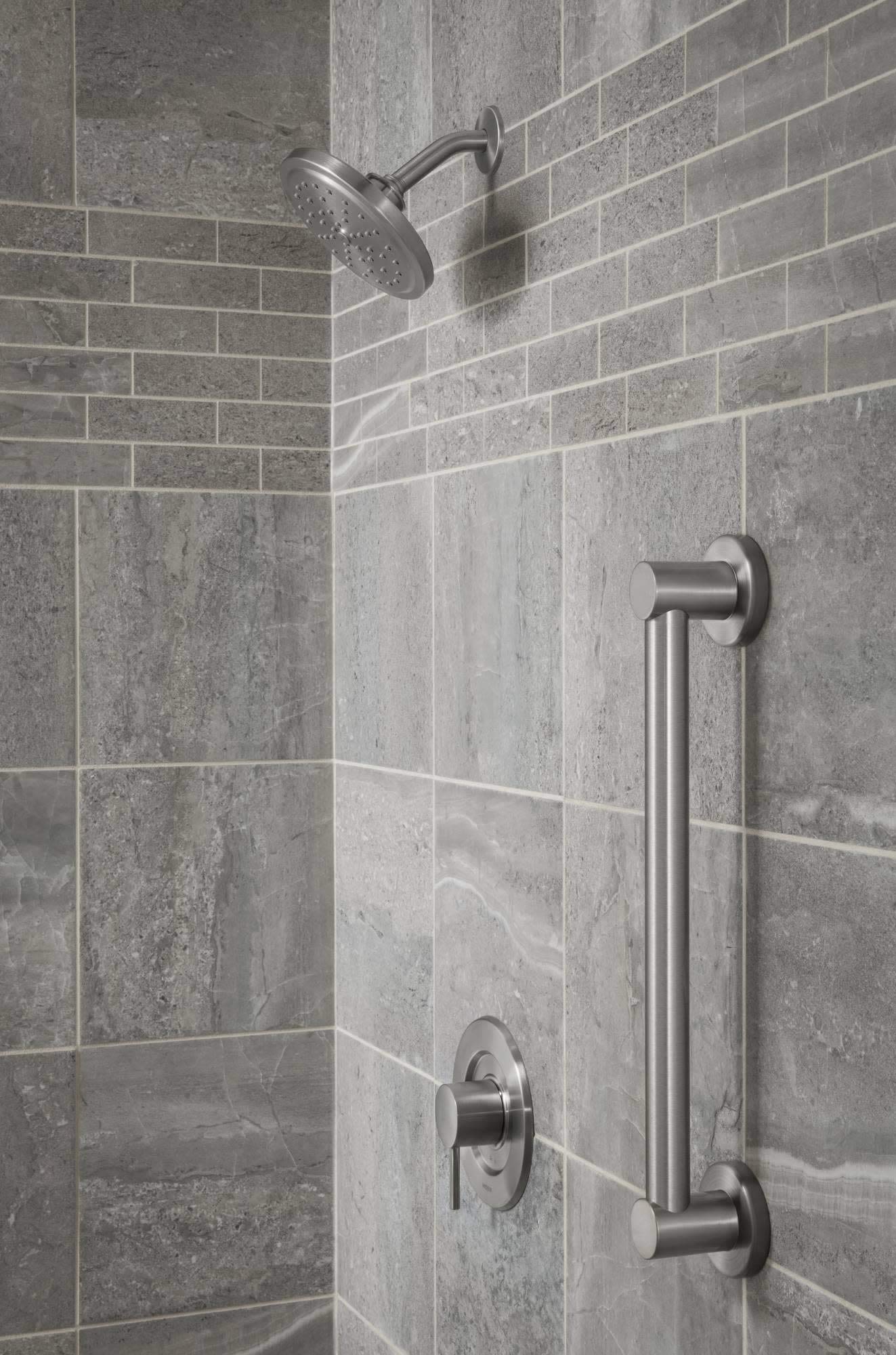 Brushed gold stainless steel grab bar mounted vertically on shower wall tile next to showerhead and controls.