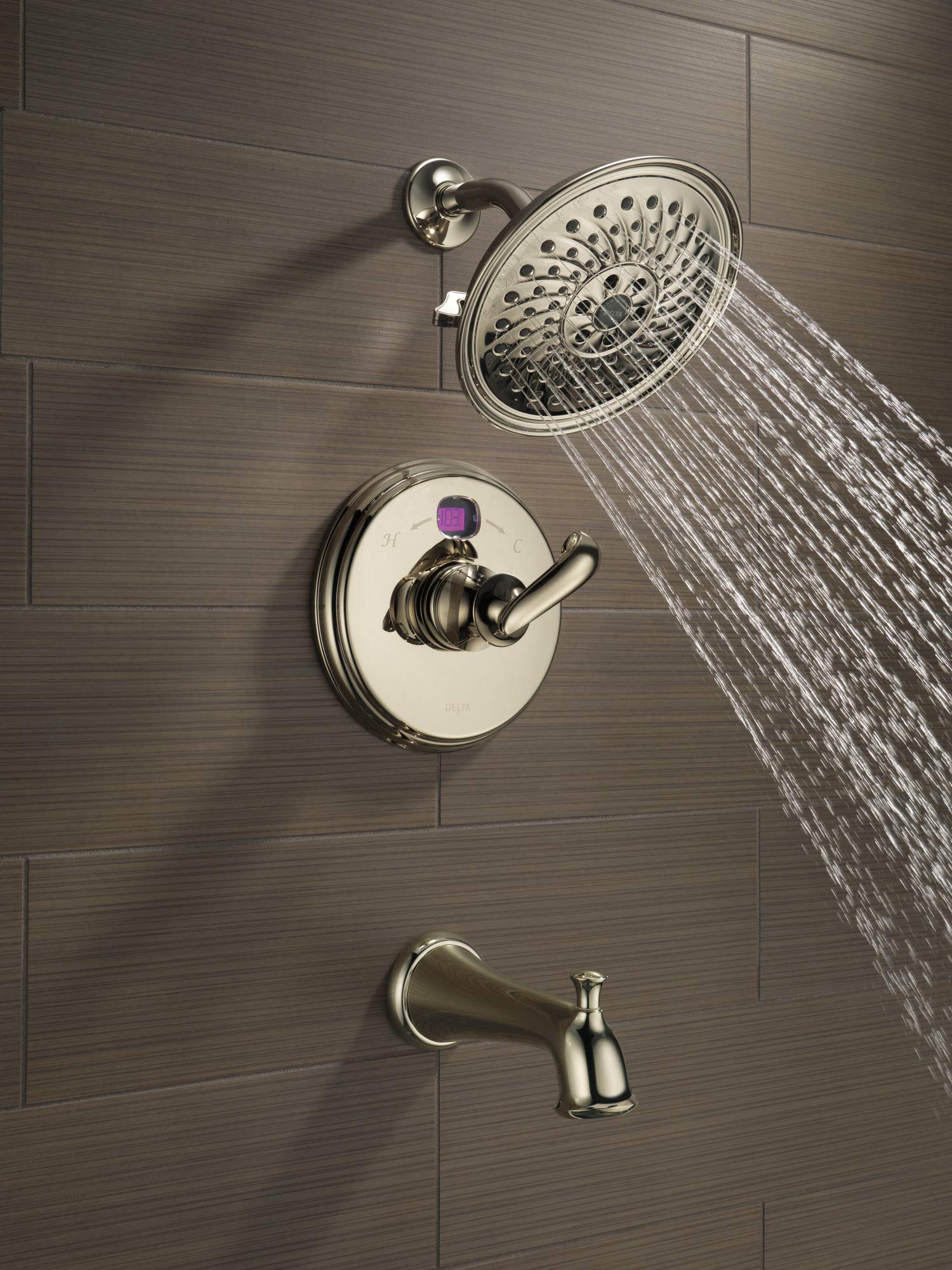 Polished nickel shower system mounted on tile wall with round showerhead, control valve, and tub spout with active water flow