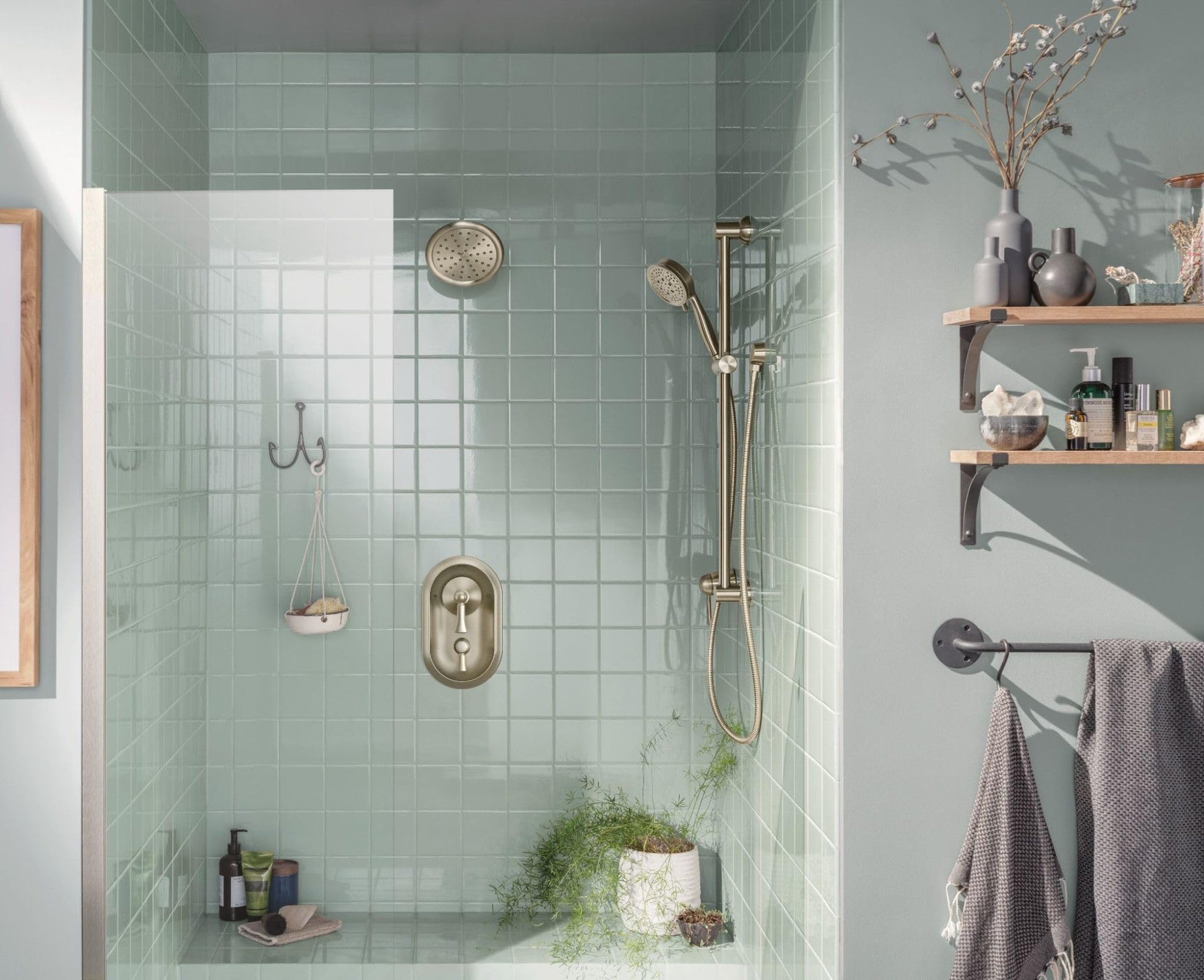 Brushed nickel shower trim kit with oval valve handle, showerhead, and handheld spray wand mounted on mint green tile wall.