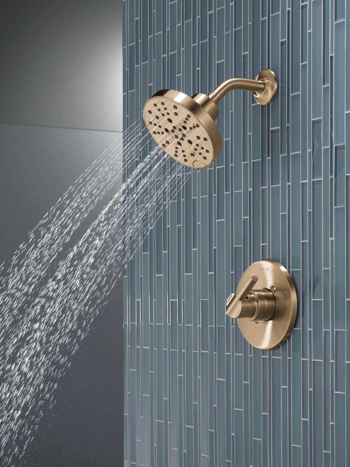 Champagne bronze shower trim with round perforated showerhead and valve control mounted on blue tile wall.