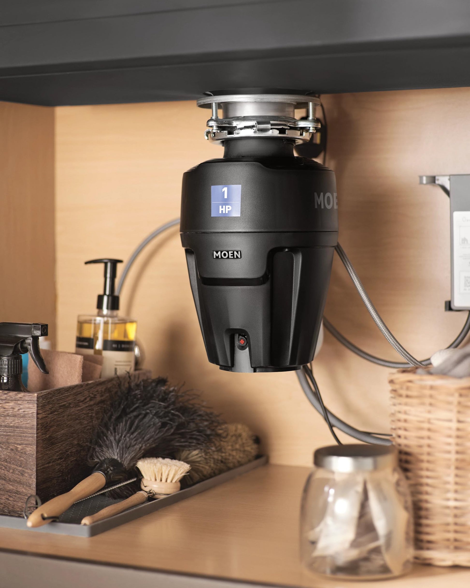 Black Moen garbage disposal with 1 HP display mounted under sink cabinet with power cord and stainless steel sink flange.