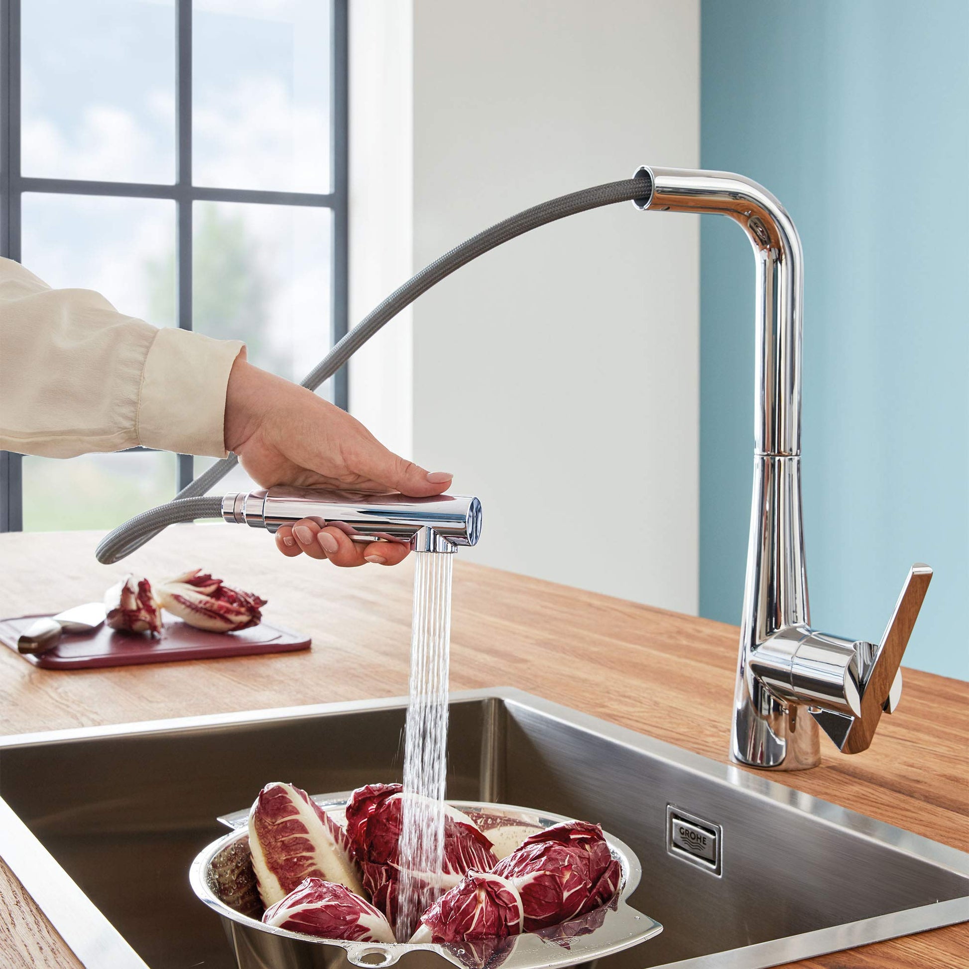 Chrome pull-out kitchen faucet with single handle and curved spout over stainless steel sink.