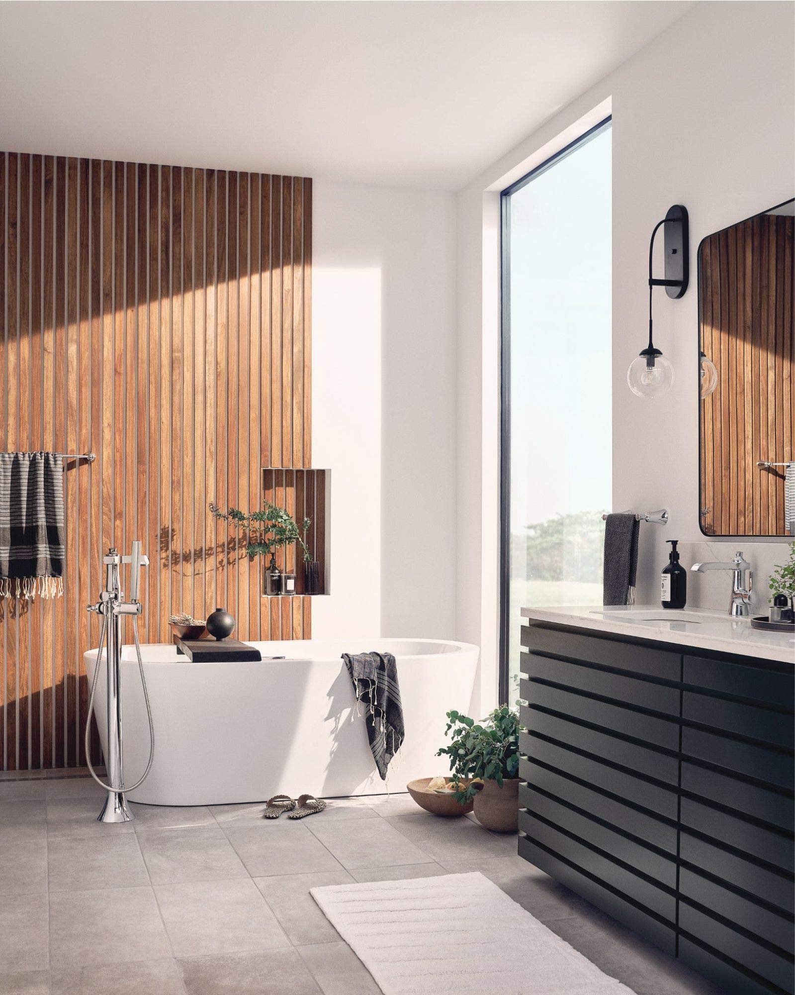 Polished nickel floor-mounted tub filler with single handle and detachable handshower installed beside a freestanding bathtub