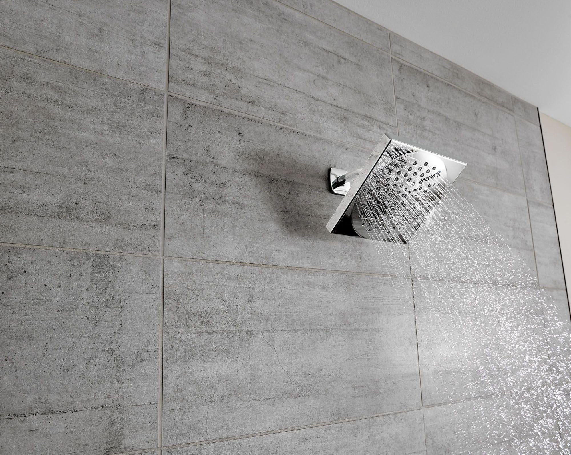 Chrome square rainshower showerhead mounted on gray tile wall with water spray visible.