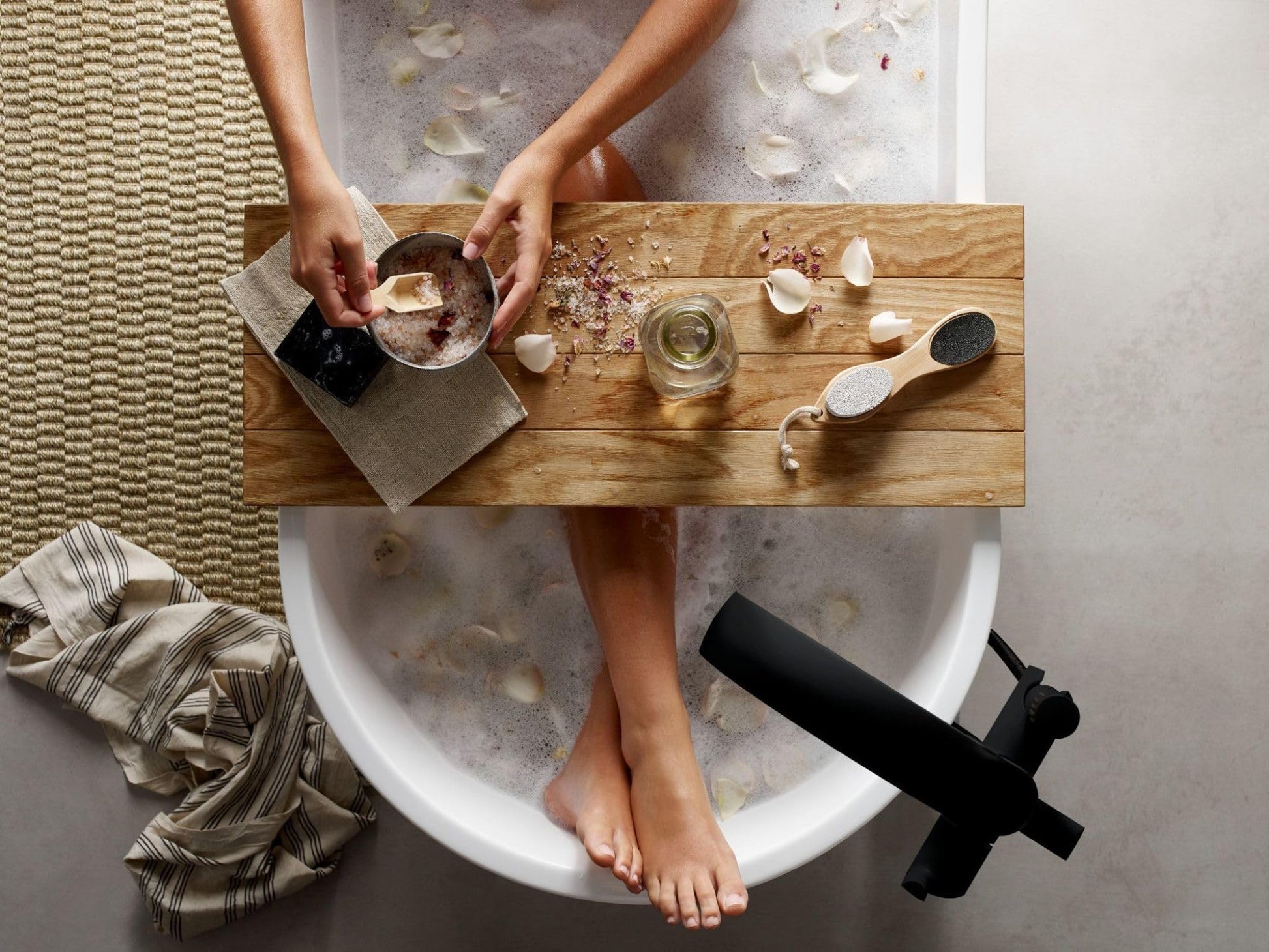 Matte black freestanding bathtub filler with single handle and detachable handshower mounted beside white soaking tub.