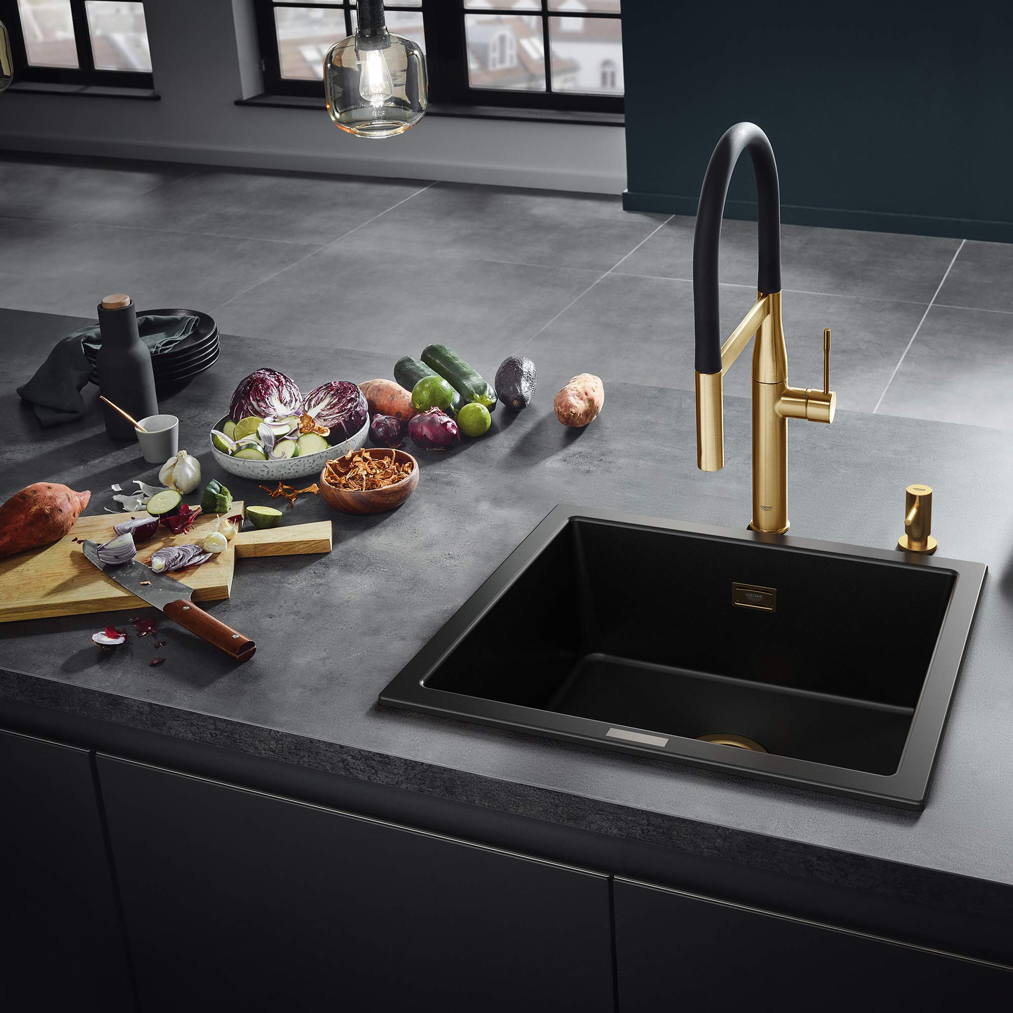 Brushed gold and black kitchen faucet with curved spout and matching soap dispenser on dark countertop.