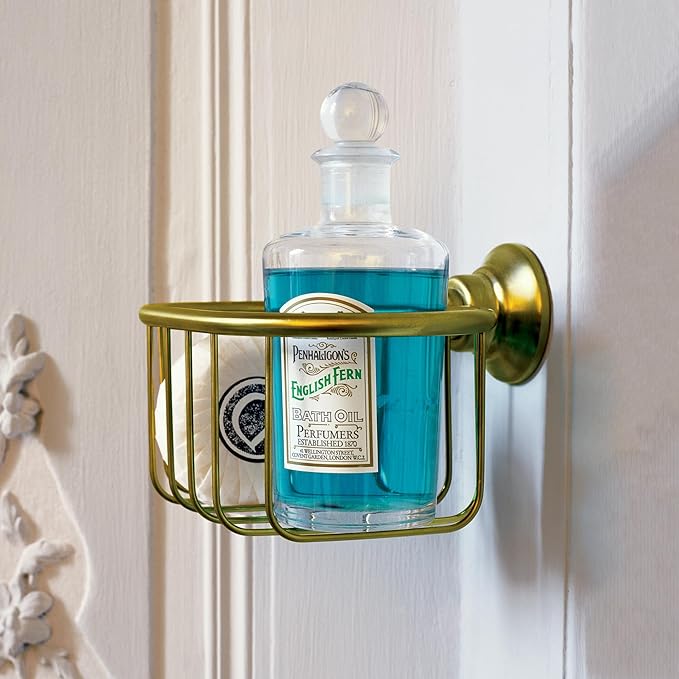 Chrome shower basket with curved sides holding a glass bottle of blue liquid, mounted on white wall tile.