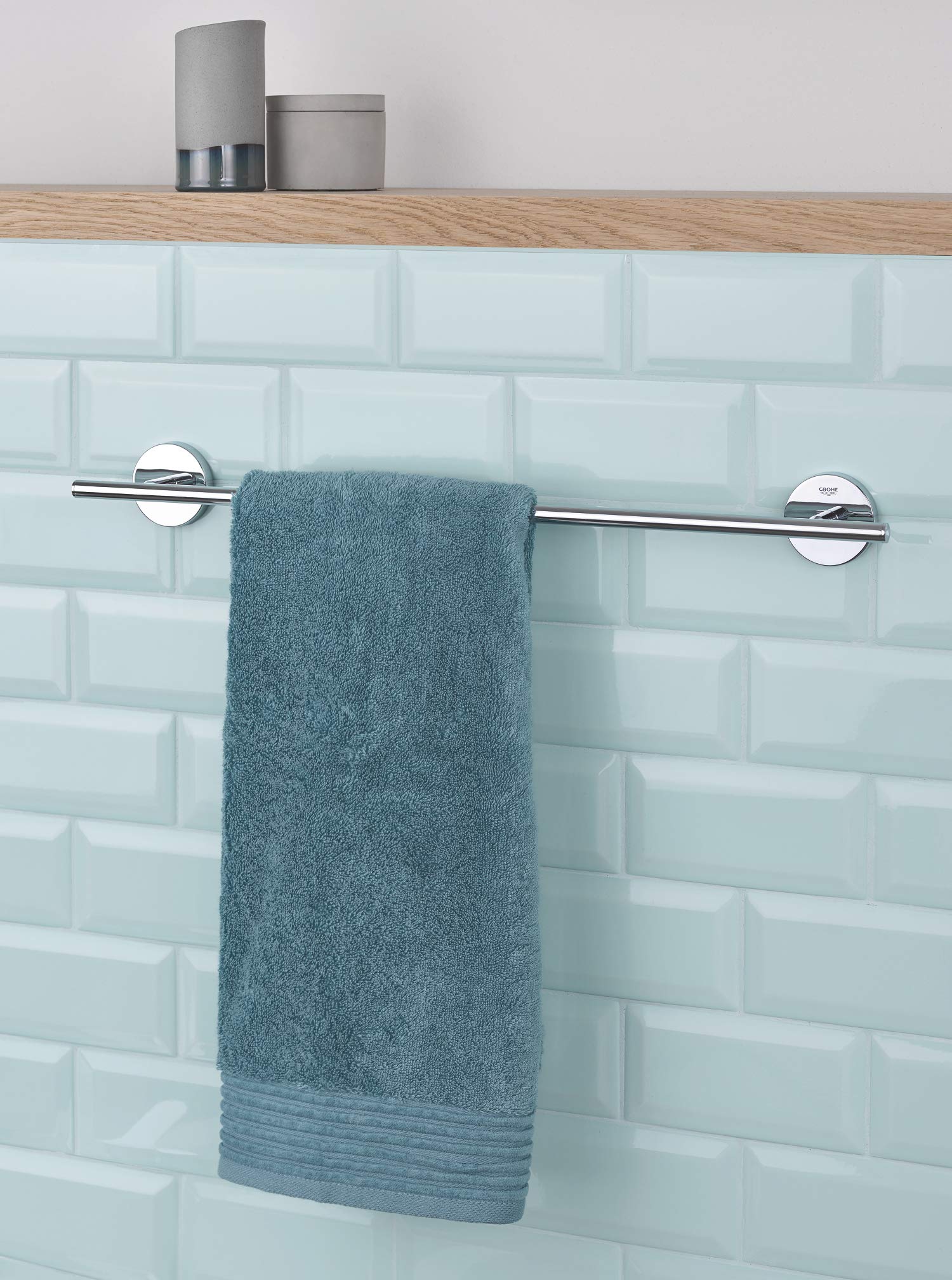 Chrome towel bar with circular wall mounts holding a folded blue-gray towel against light tile bathroom wall.