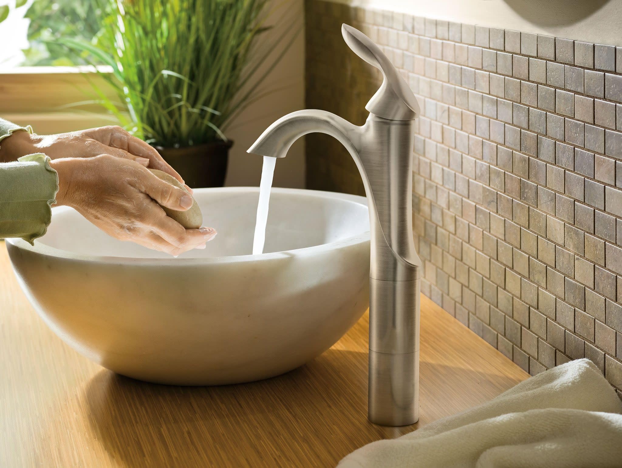 Chrome single-handle bathroom faucet with tall curved spout over white vessel sink.