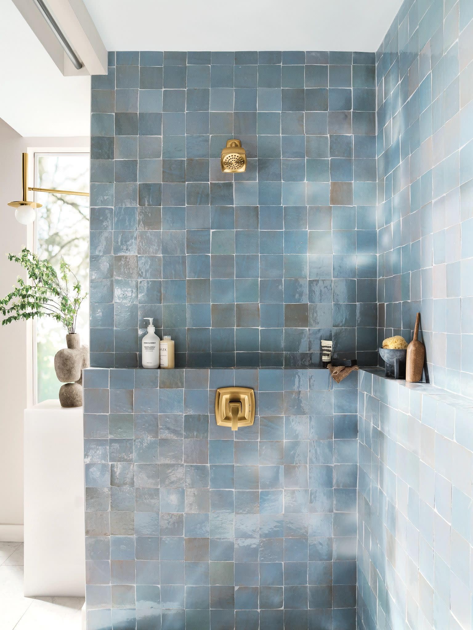 Gold-finish shower valve trim with round handle mounted on blue tile wall.