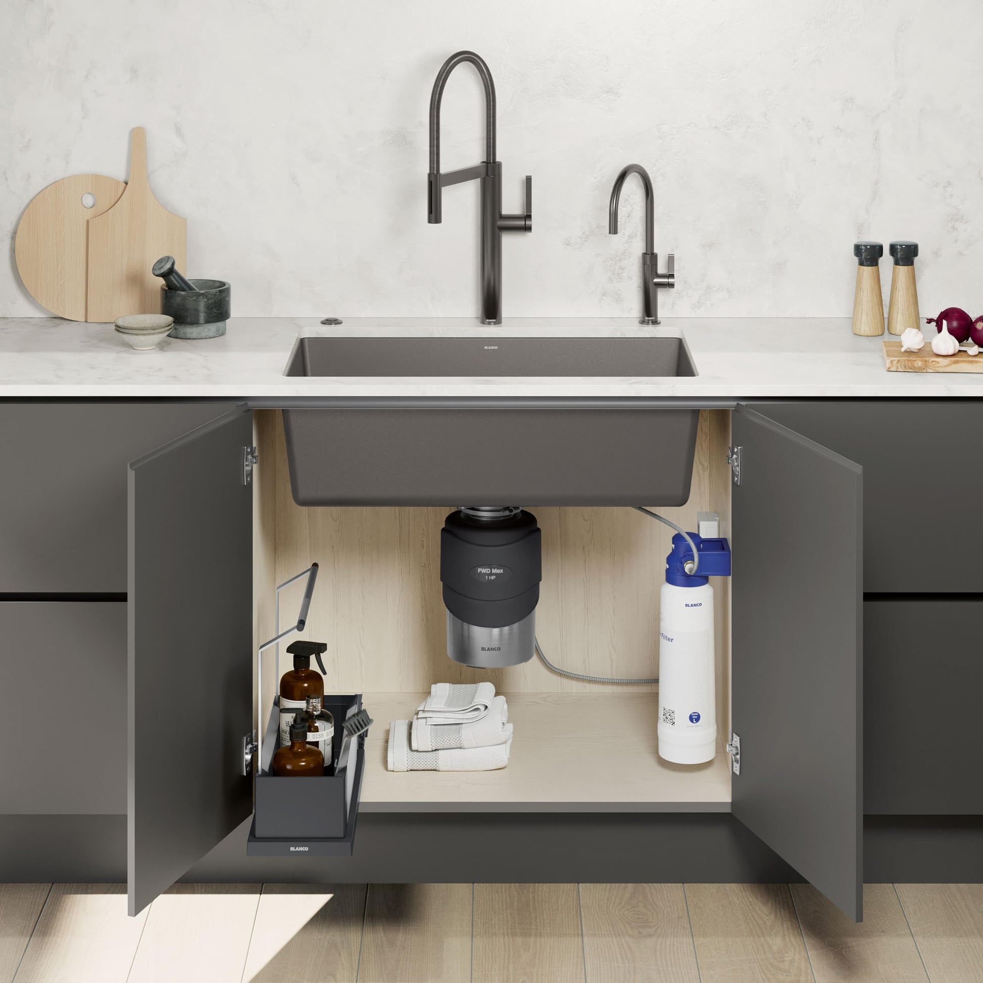 Black food waste disposal unit installed under kitchen sink with gray composite basin and plumbing components visible.