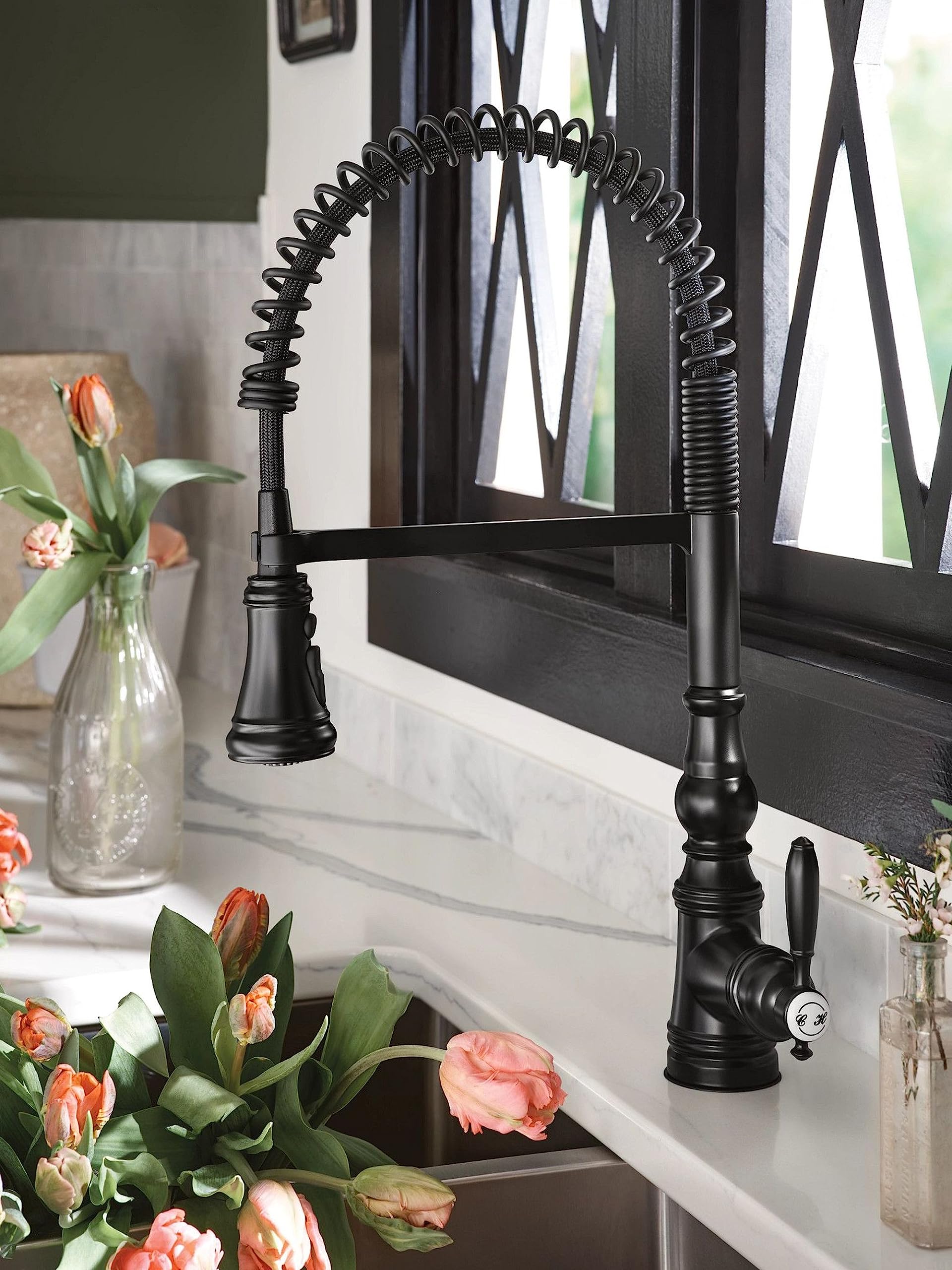 Matte black pulldown kitchen faucet with coiled spring hose and single handle control mounted above sink.