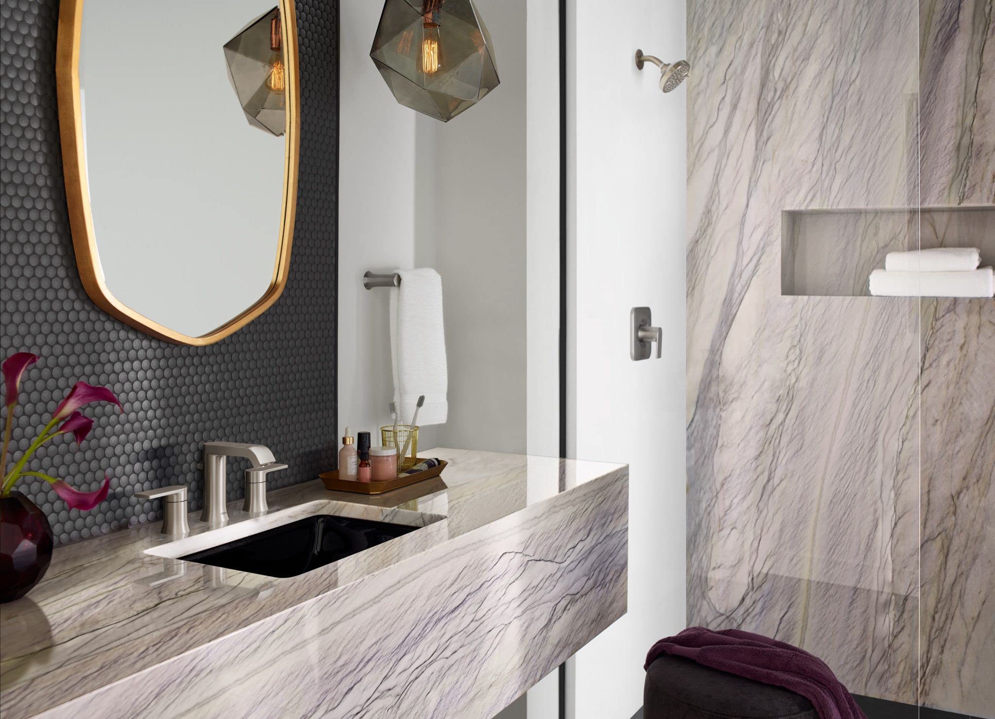 Brushed nickel hand towel bar mounted vertically on white bathroom wall above marble countertop.