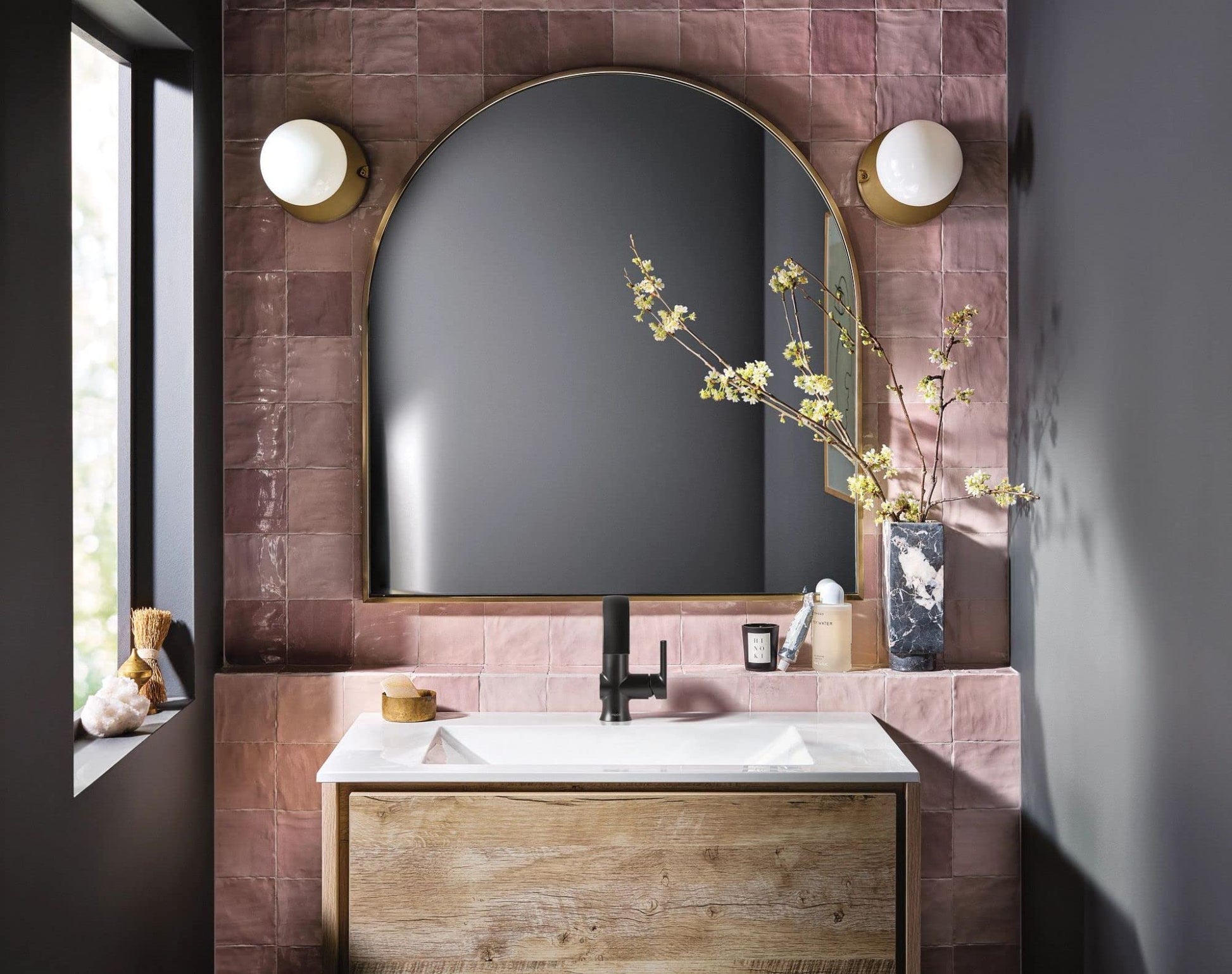 Matte black single-handle bathroom faucet with high arc spout installed on white sink in mauve tile bathroom.