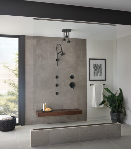 Matte black ceiling-mounted showerhead with cylindrical body and circular spray plate mounted above shower enclosure.