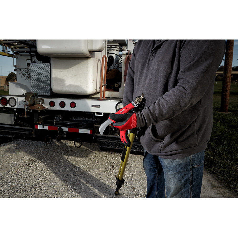 Lineman's hawkbill knife with red handle and metal ring attachment, held in hand near utility truck.