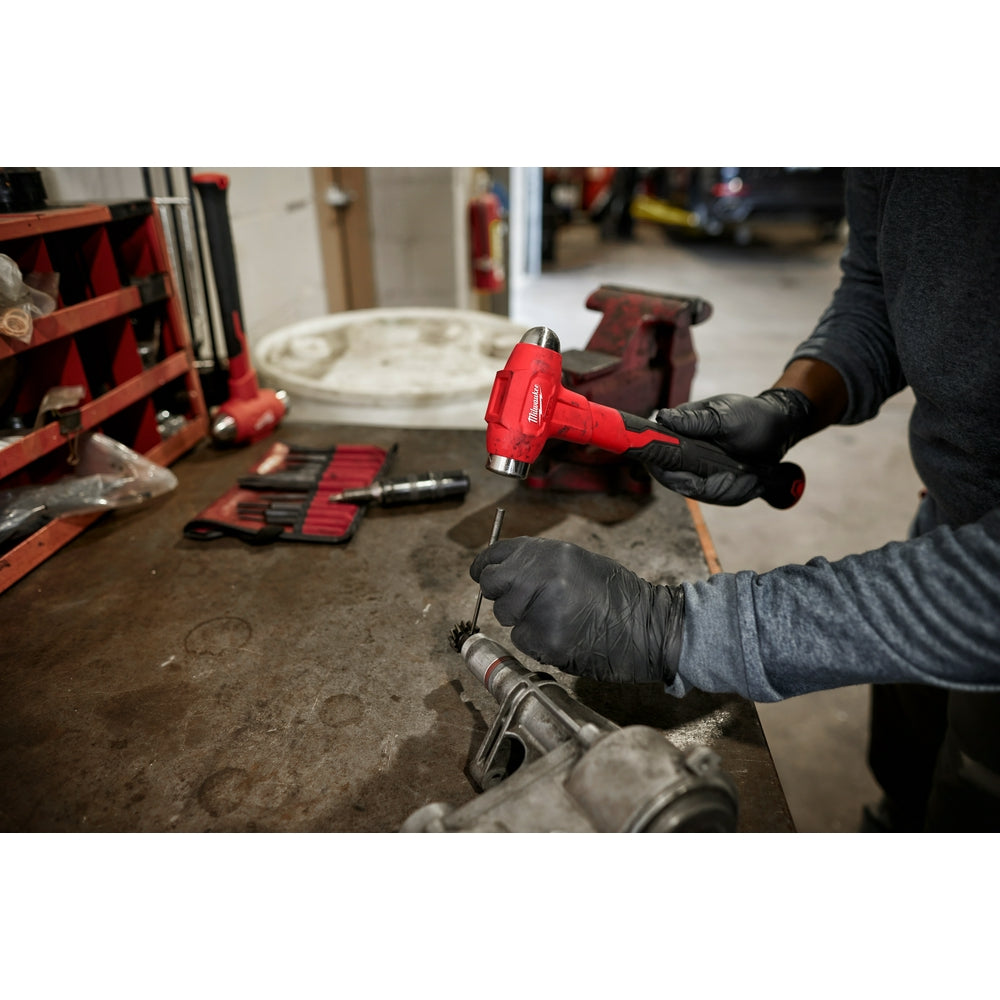 Red and black Milwaukee dead blow hammer with ball peen head held in worker's gloved hands in workshop setting.