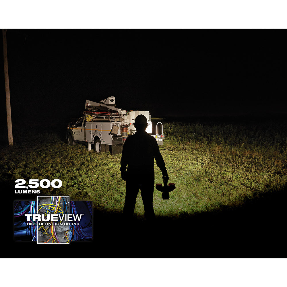 Person holding Milwaukee M18 bucket light illuminating a utility truck at night with 2,500 lumens output.