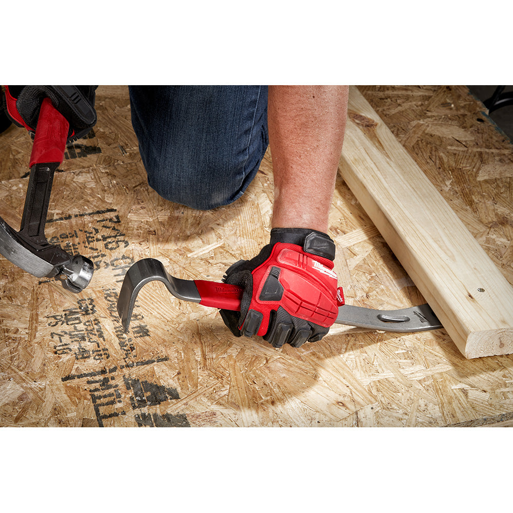 Black and red pry bar with curved claw end held in hand over wooden surface.